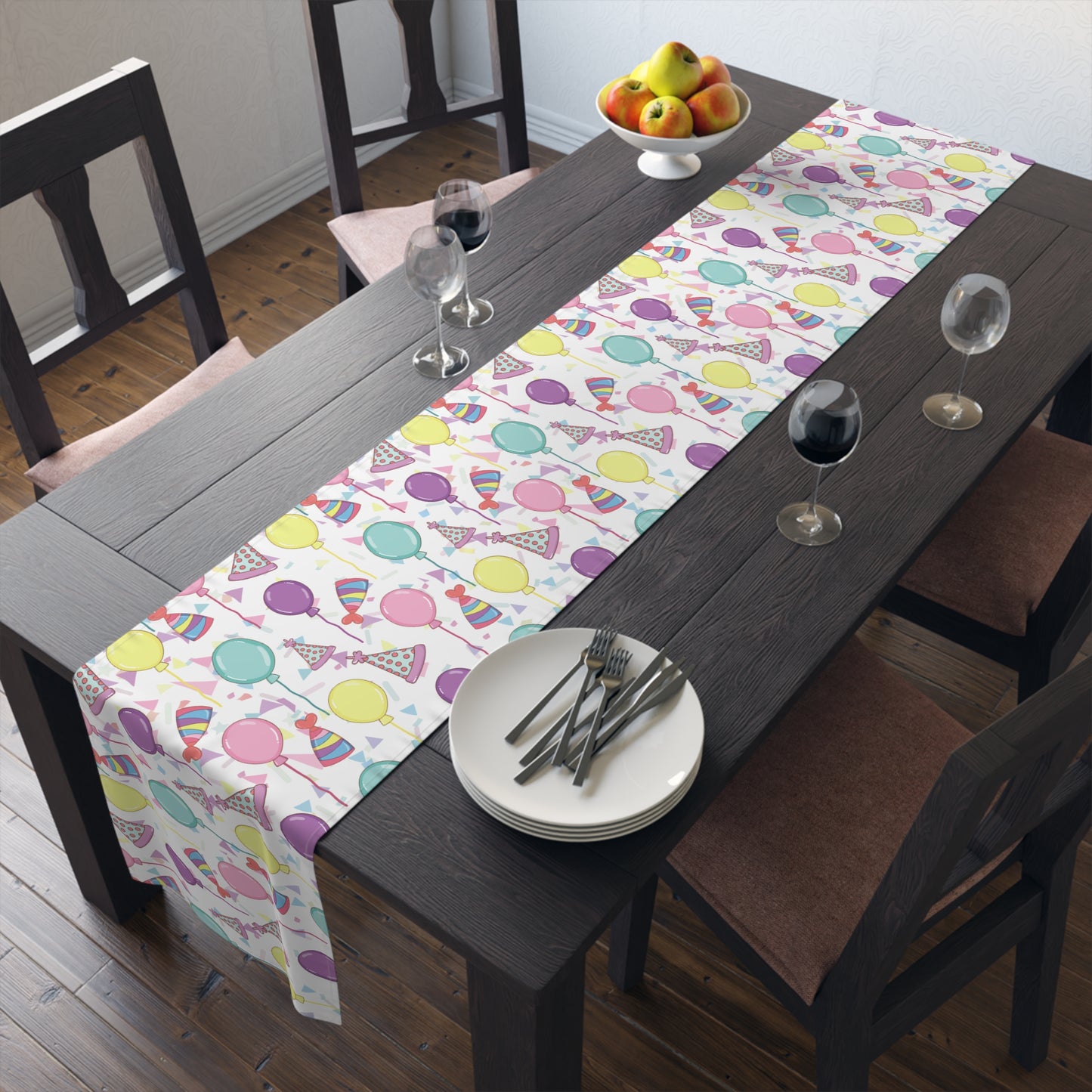 Table runner with birthday hats, confetti and purple, yellow, blue and pink balloons on a white background on a dark wood table