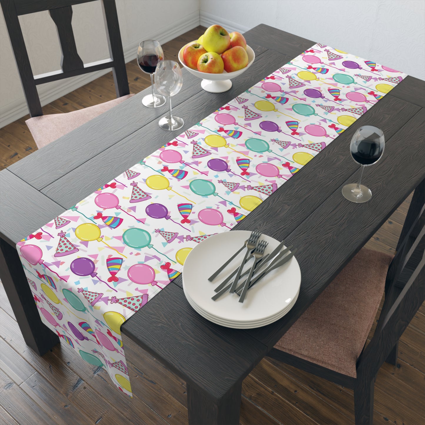 Table runner with birthday hats, confetti and purple, yellow, blue and pink balloons on a white background on a dark wood table