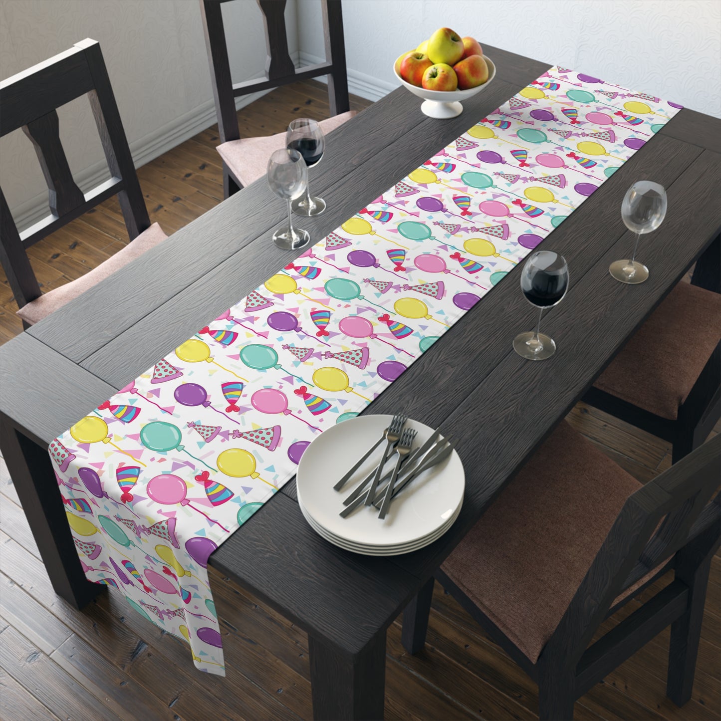 Table runner with birthday hats, confetti and purple, yellow, blue and pink balloons on a white background on a dark wood table