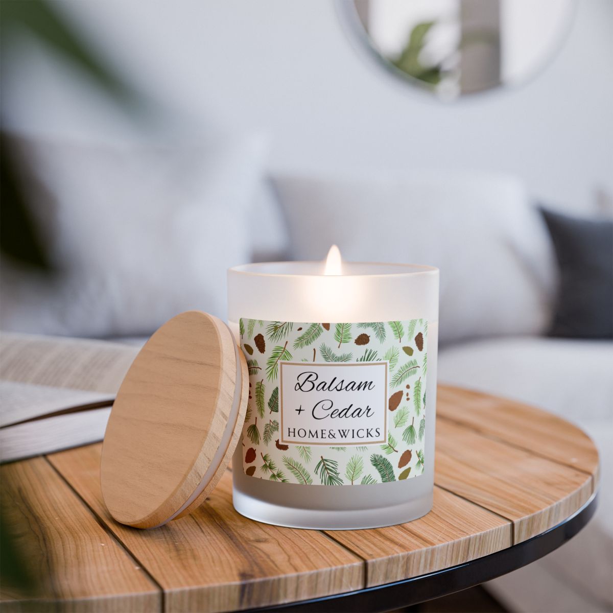 Lit wood wick candle with 'Balsam + Cedar' label with cones and cedar leaves on a white background by Home & Wicks with a decorative label on a wooden table, blurred background