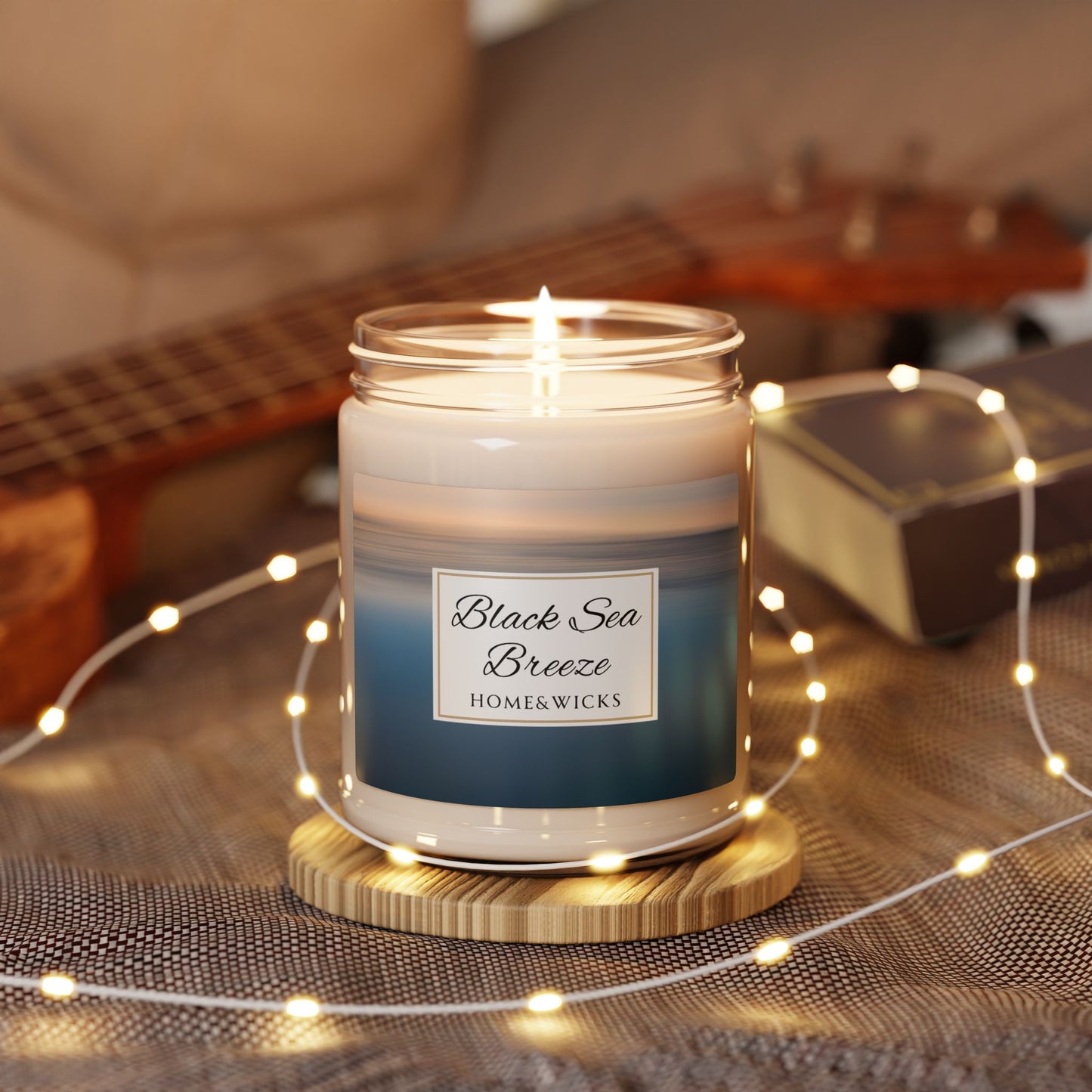 Homewares candle labeled 'Black Sea Breeze' by Home & Wicks on a wooden coaster with string lights.