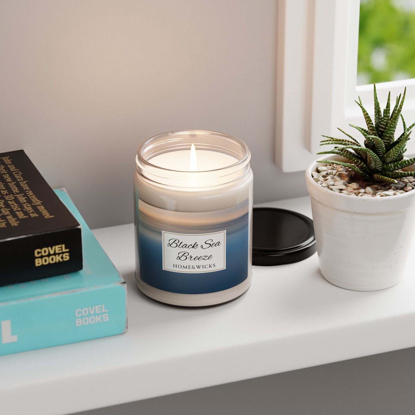 Candle labeled 'Black Sea Breeze' on a shelf with books and a plant