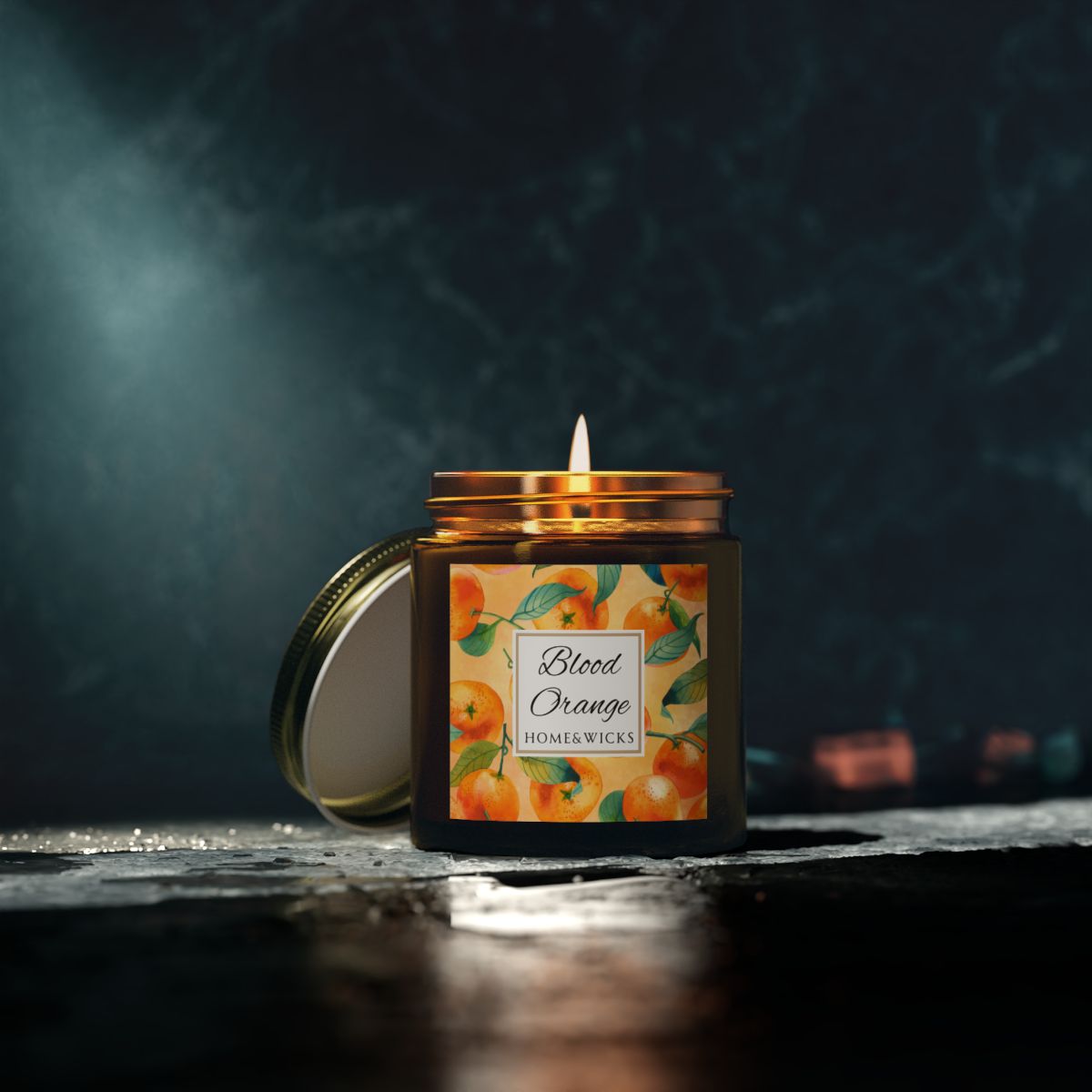 Blood Orange candle in an amber glass jar with gold lid with 'Blood Orange' label featuring oranges illustration on a white background by Home & Wicks on a dark background