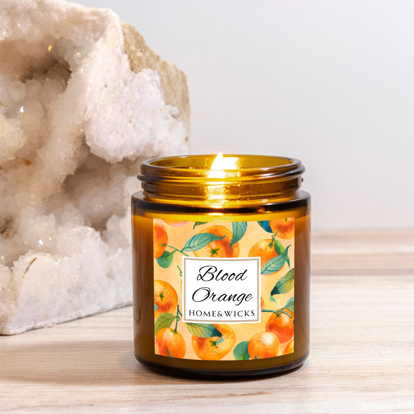 Blood Orange candle in an amber glass jar with gold lid with 'Blood Orange' label featuring oranges illustration on a white background by Home & Wicks placed against a white background.