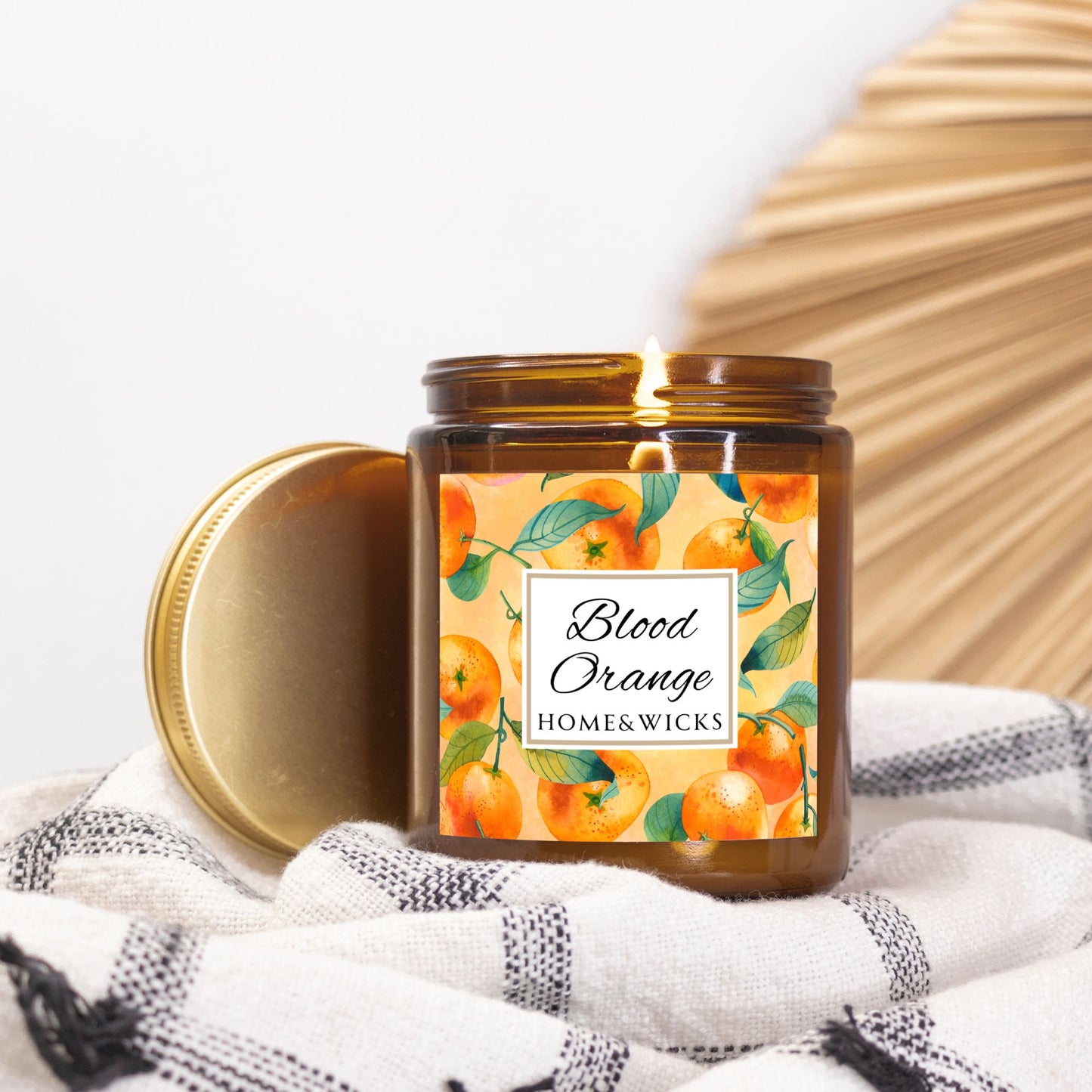 Blood Orange cotton wicked apricot coconut wax candle in an amber jar with gold lid and with 'Blood Orange' label and orange design on a white background by Home & Wicks on a white and black patterned fabric background
