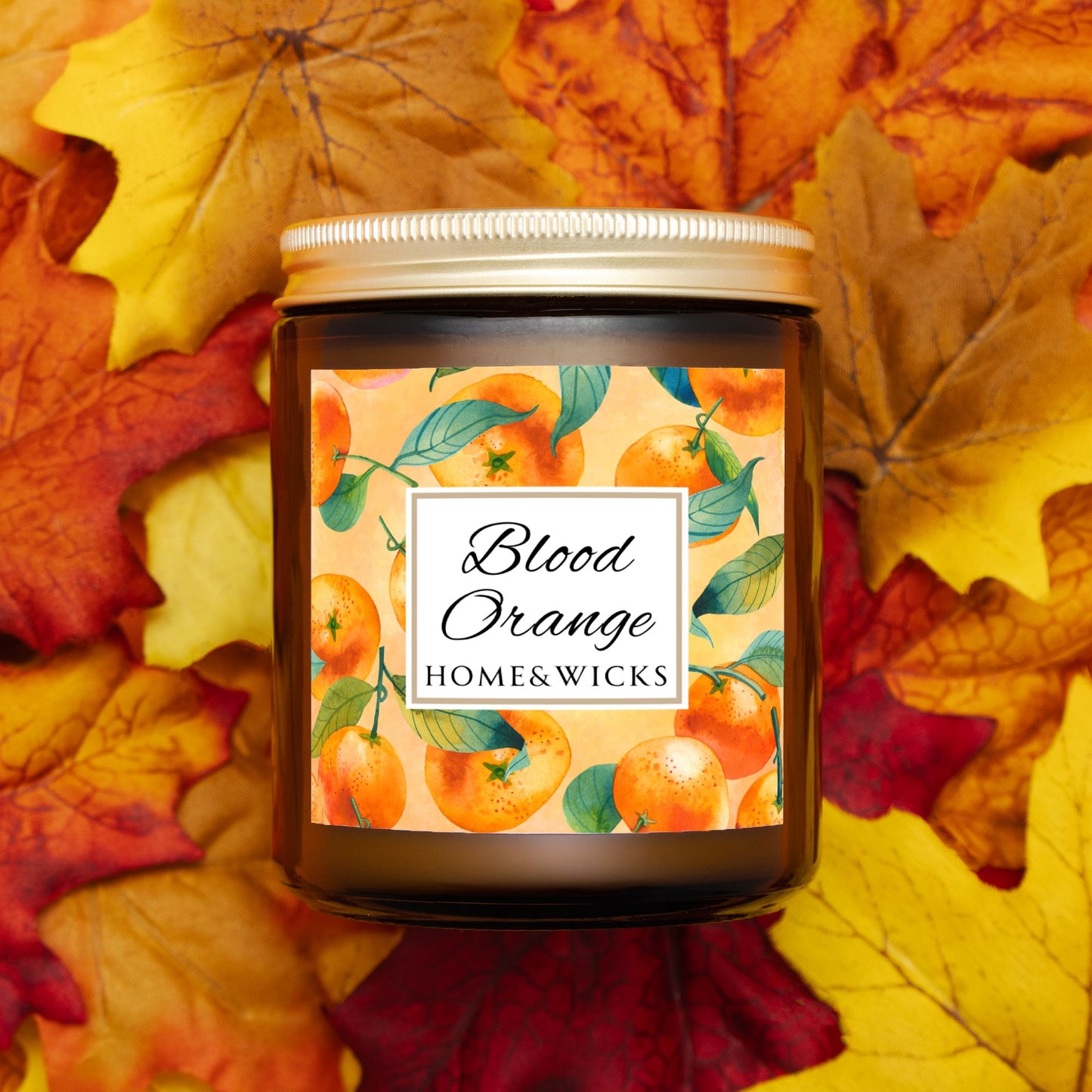 Blood Orange cotton wicked apricot coconut wax candle in an amber jar with gold lid and with 'Blood Orange' label and orange design on a white background by Home & Wicks on a background of autumn leaves.