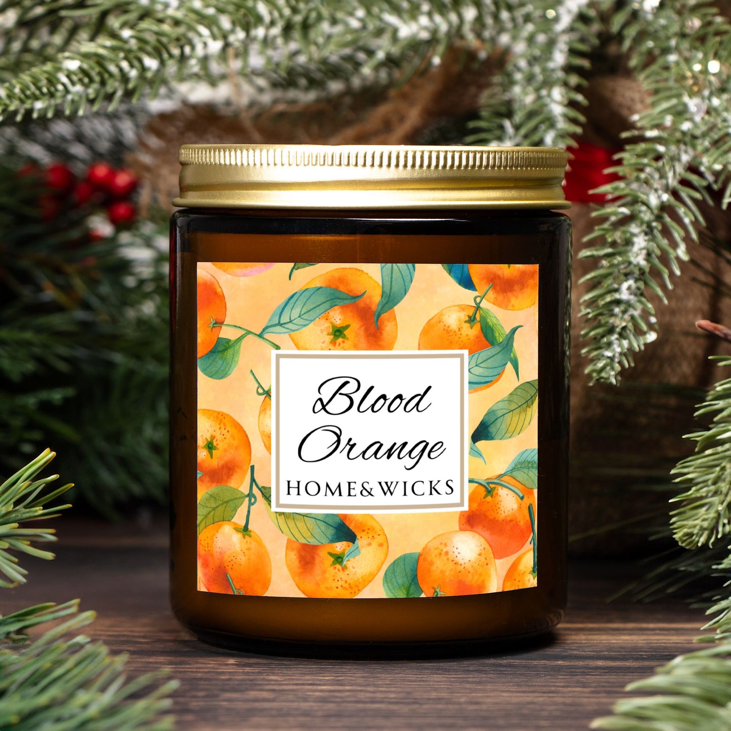 Blood Orange cotton wicked apricot coconut wax candle in an amber jar with gold lid and with 'Blood Orange' label and orange design on a white background by Home & Wicks with a decorative background of greenery and berries.