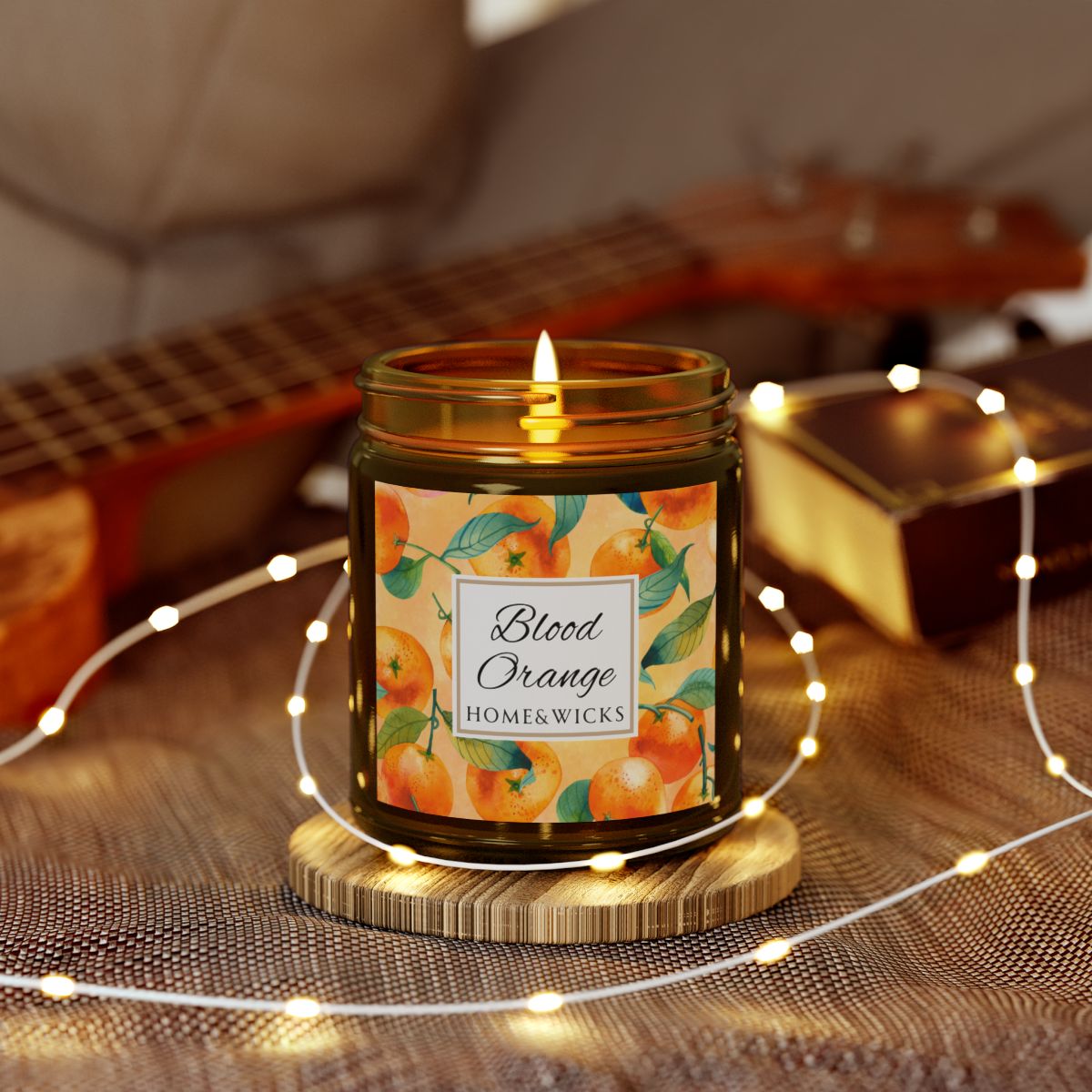 Blood Orange cotton wicked apricot coconut wax candle in an amber jar with gold lid and with 'Blood Orange' label and orange design on a white background by Home & Wicks surrounded by string lights on a textured surface.