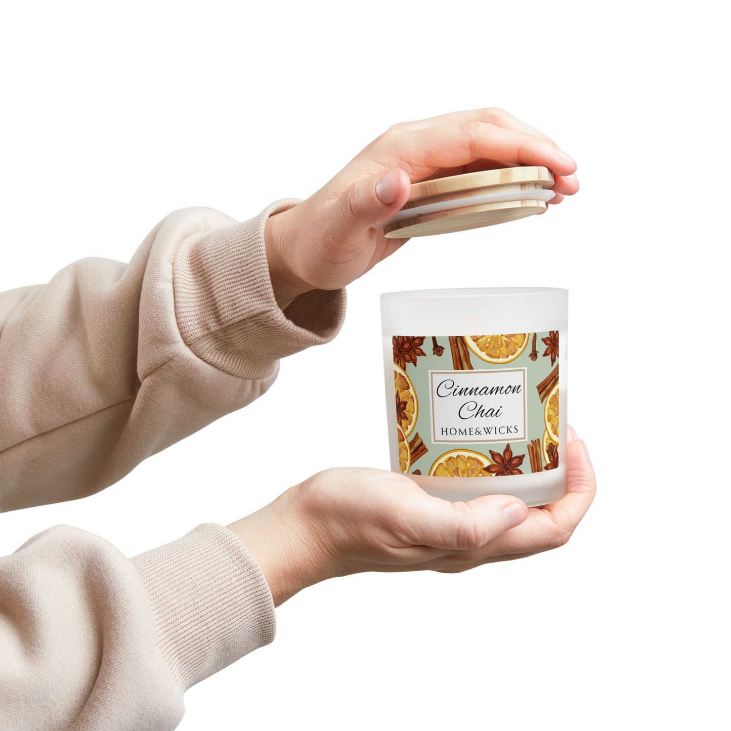 Person holding a 'Cinnamon Chai' candle with a decorative label on a white background