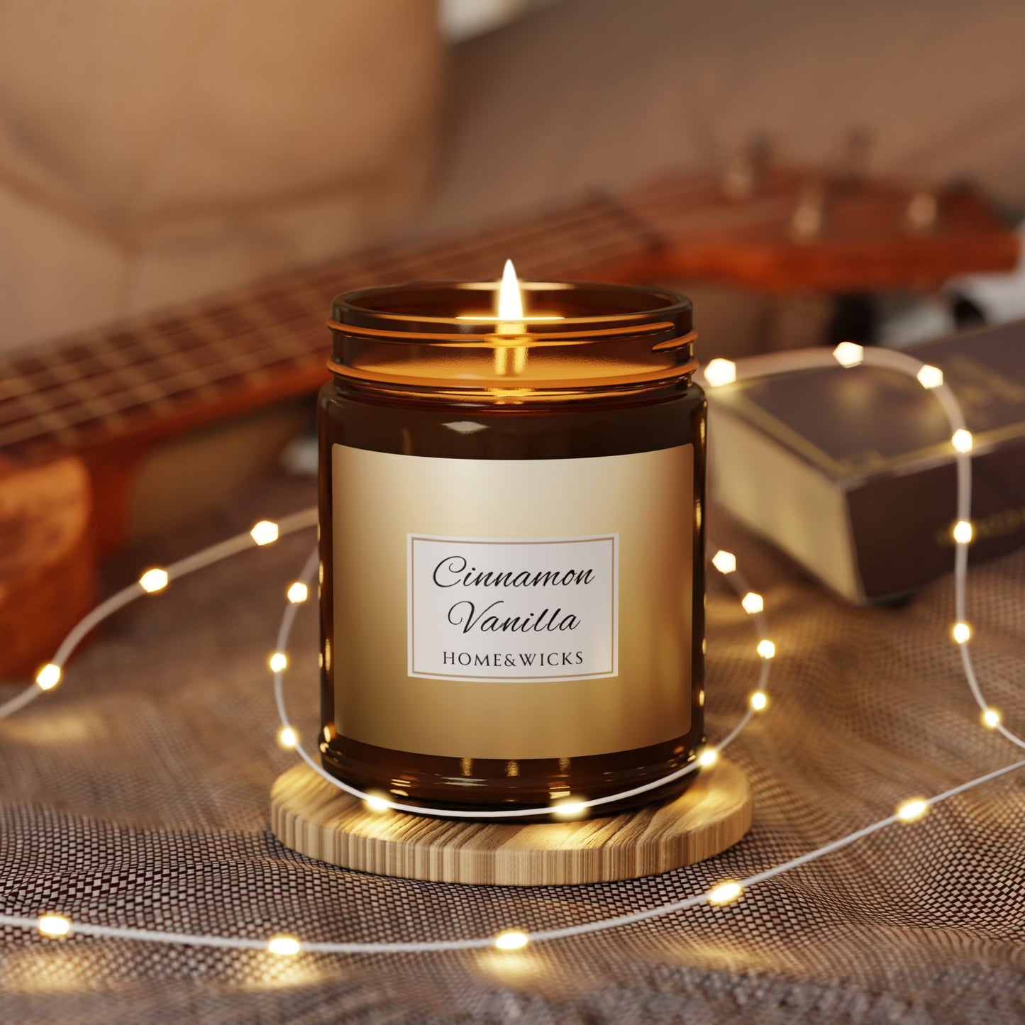 Candle labeled 'Cinnamon Vanilla' by Home & Wicks on a wooden coaster with string lights and a guitar in the background.