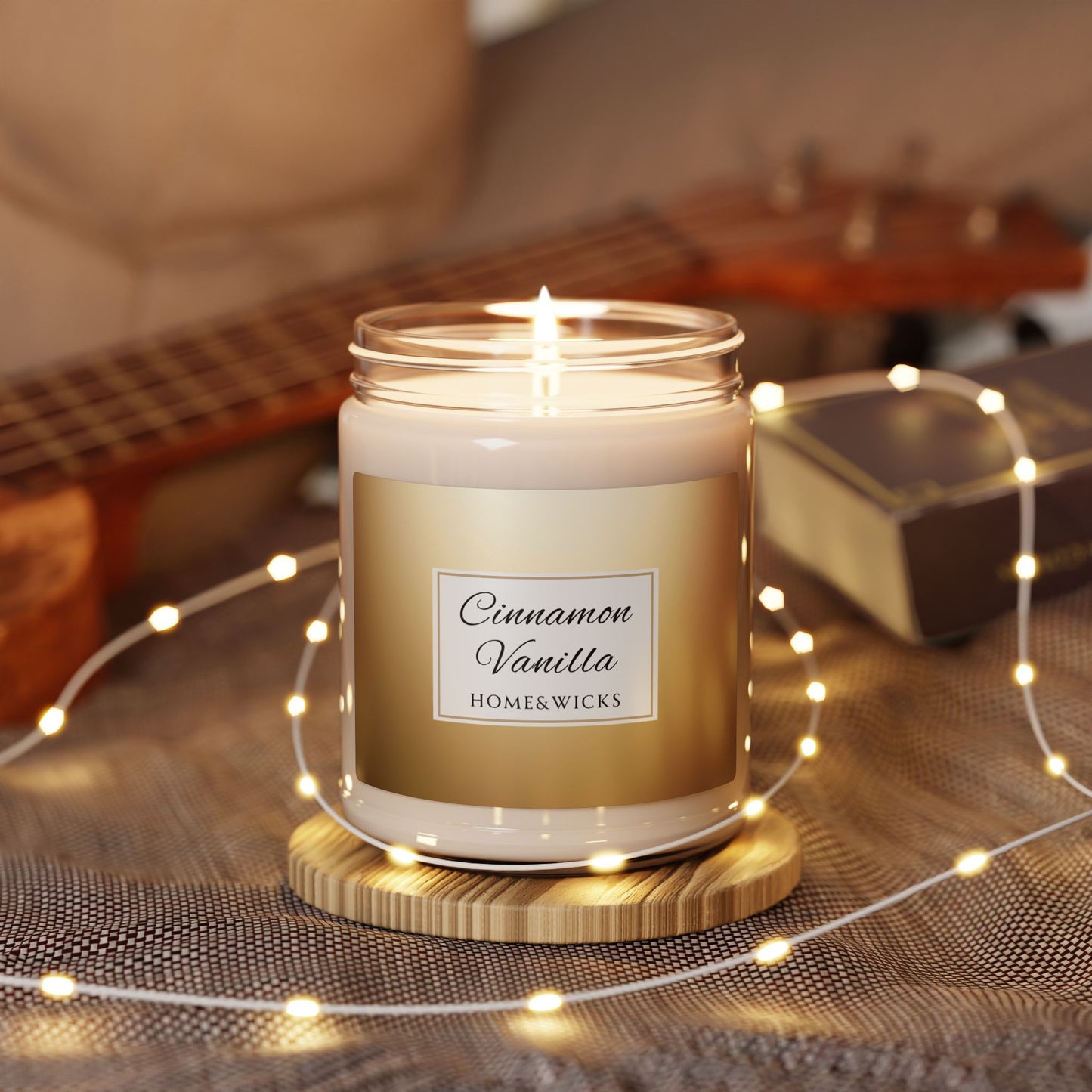 Candle labeled 'Cinnamon Vanilla' by Home&Wicks on a wooden coaster with string lights and a guitar in the background.