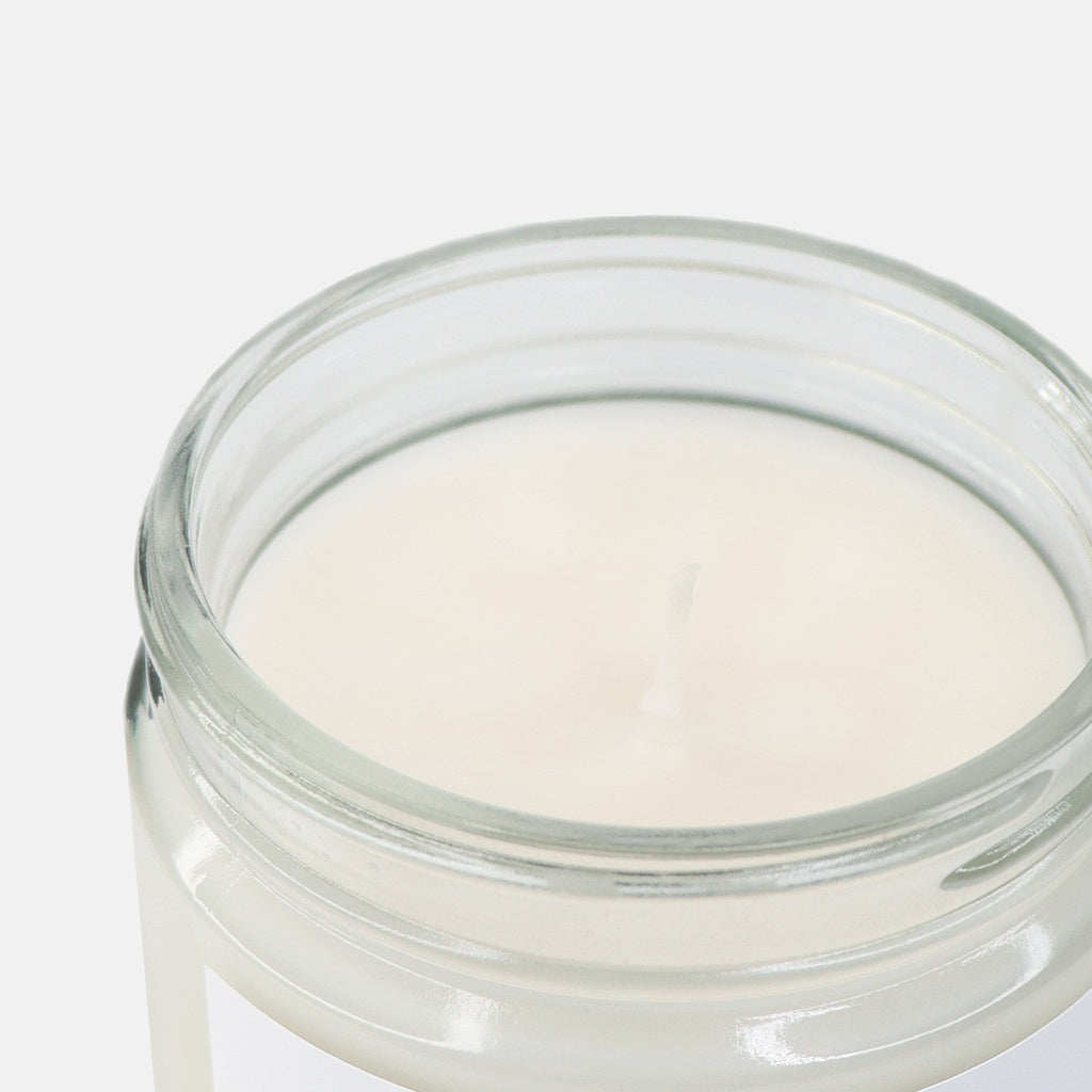 Cotton wick in clear candle glass jar with white creamy wax inside on a white background