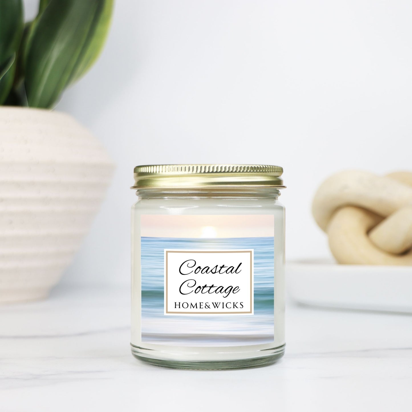 Coastal Cottage candle in clear jar with gold lid with a 'Coastal Cottage Home & Wicks' label with ocean shore image on a white background on a light background