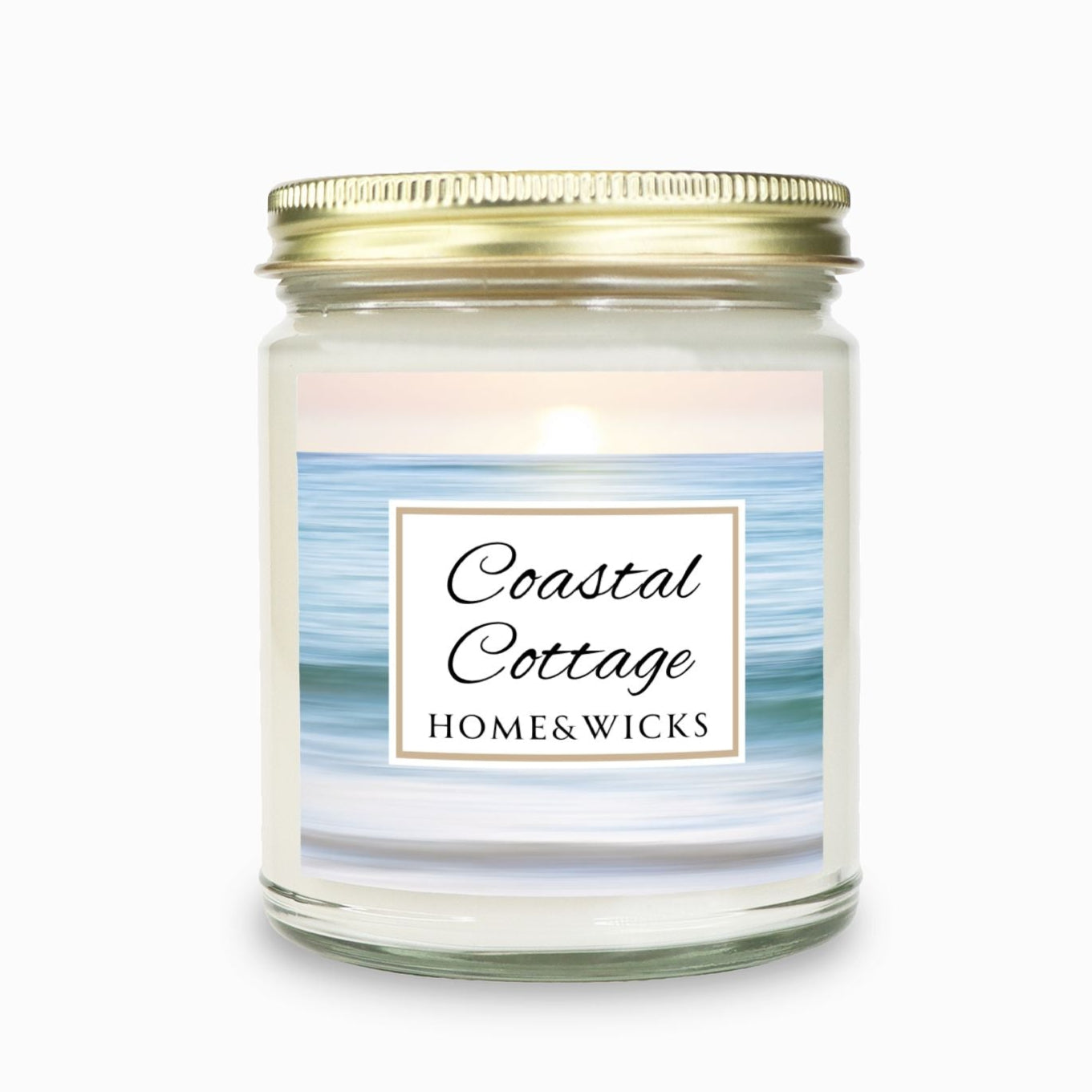 Coastal Cottage candle in clear jar with gold lid with a 'Coastal Cottage Home & Wicks' label with ocean shore image on a white background