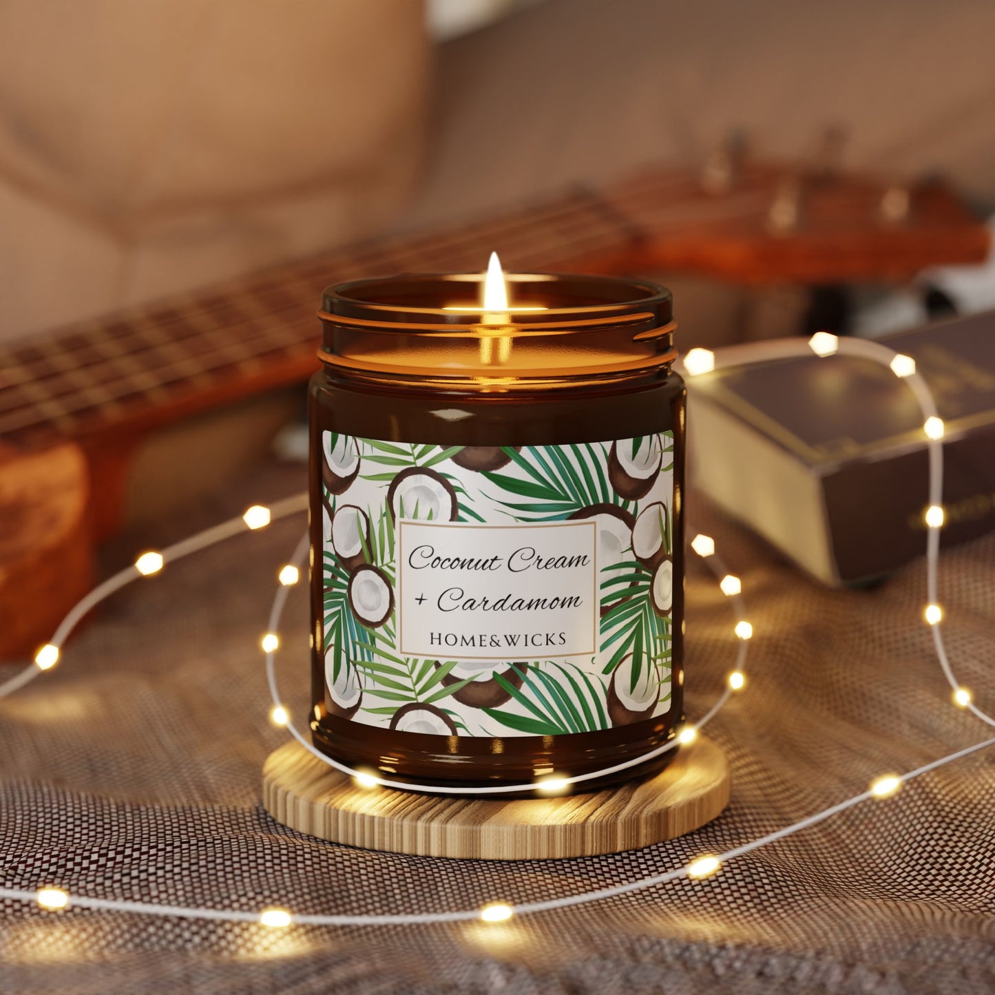 Candle in a jar labeled 'Coconut Cream + Cardamom' by Homekwick on a wooden coaster with string lights and a guitar in the background.