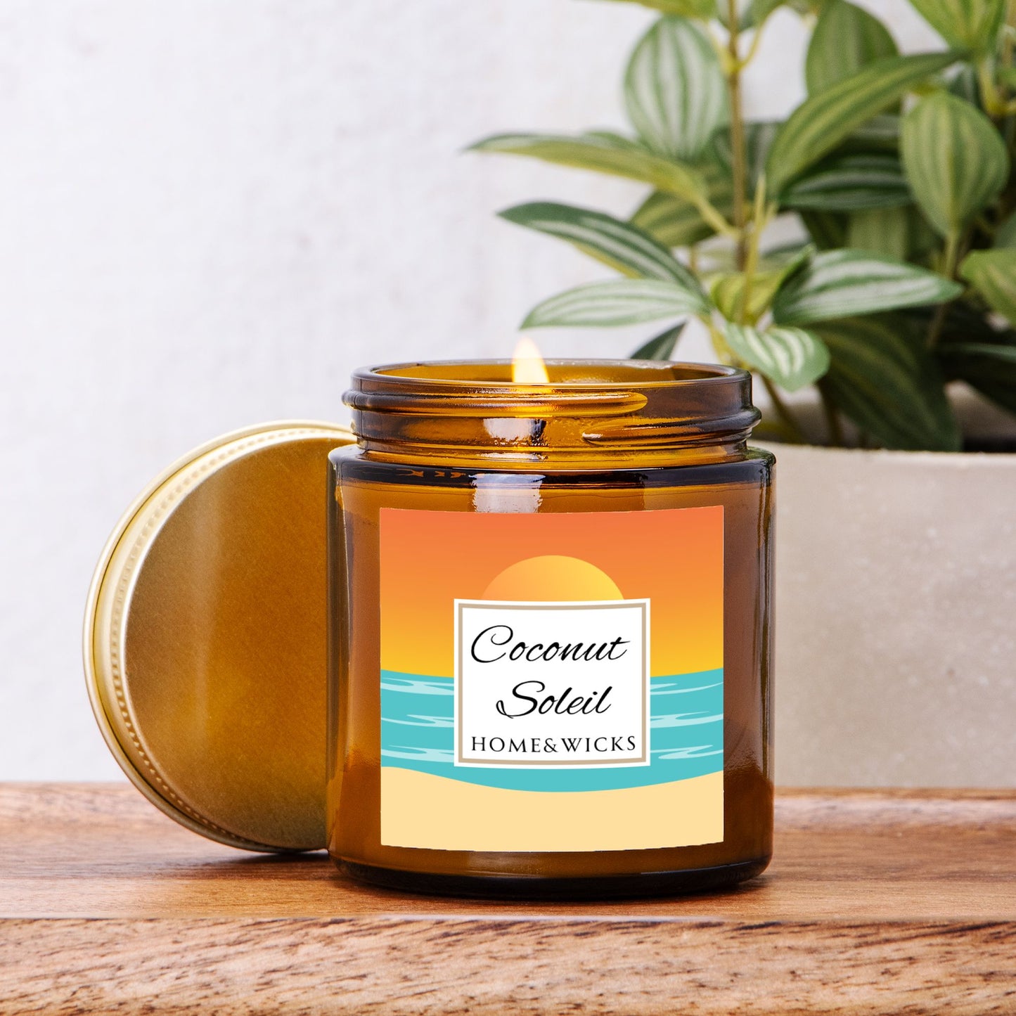 Coconut Soleil candle in 4 oz. amber glass jar with gold lid with a colorful sunset label on a white background by Home & Wicks on a wooden surface, plant in the background