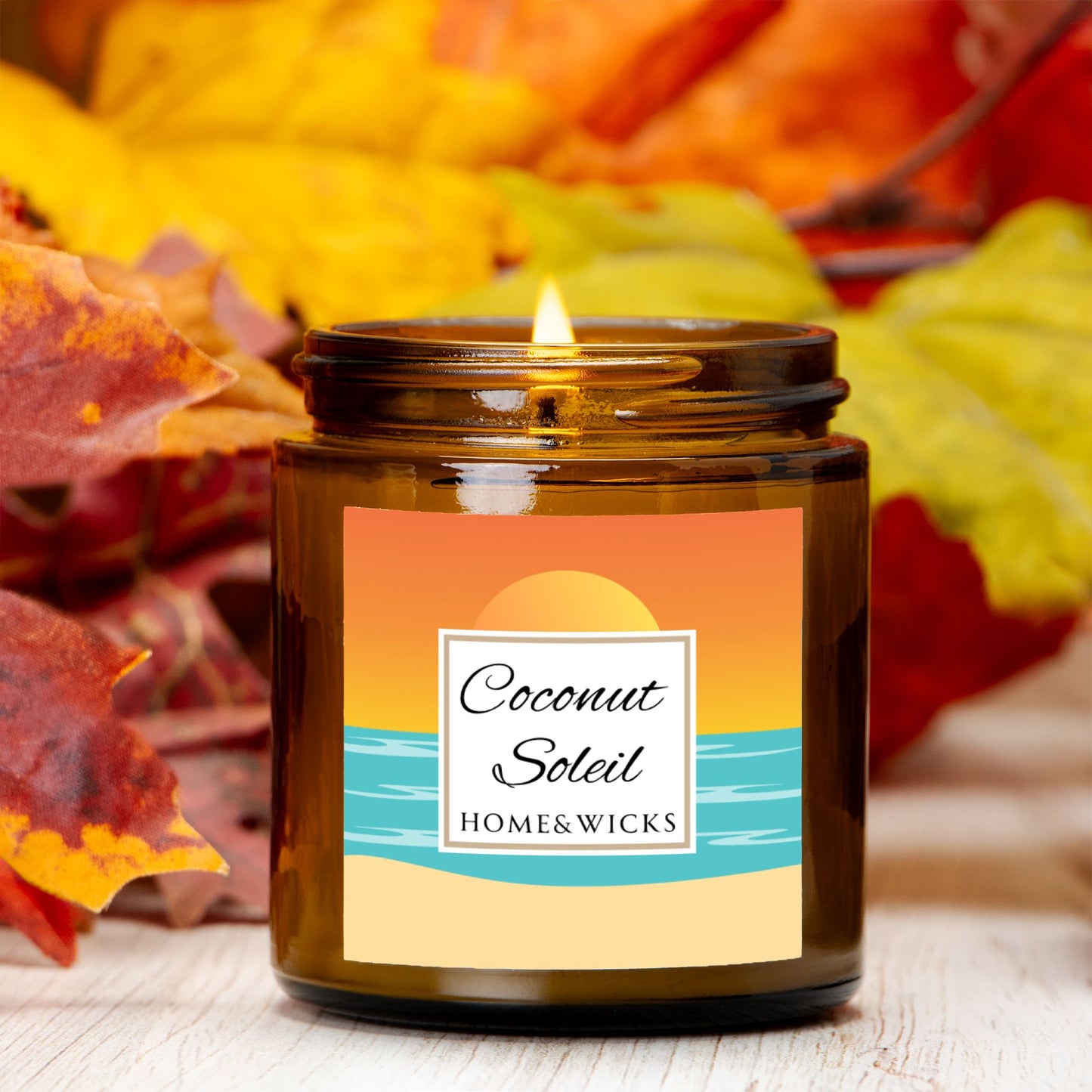 Coconut Soleil candle in 4 oz. amber glass jar with gold lid with a colorful sunset label on a white background by Home & Wicks surrounded by autumn leaves.