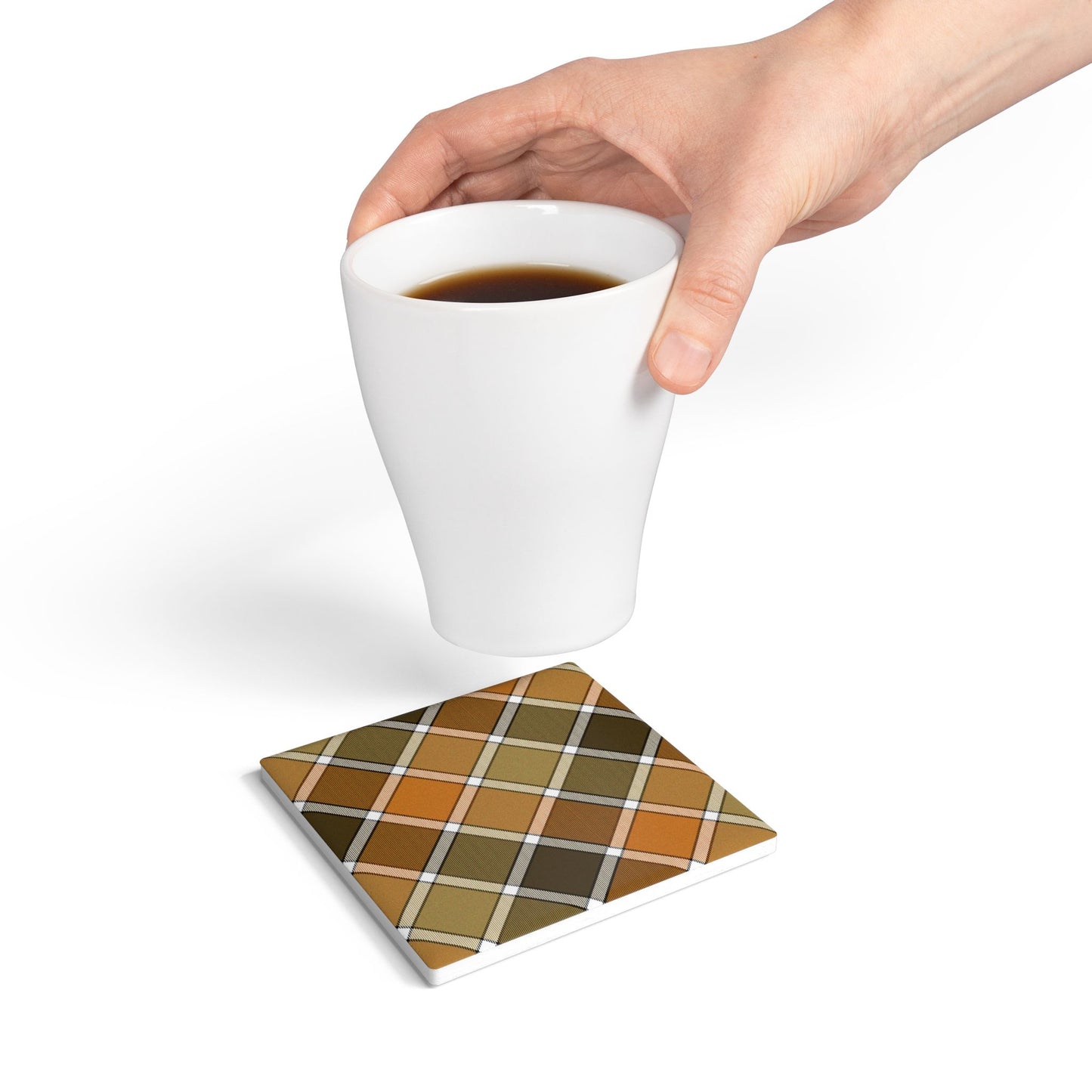Hand holding a white mug with a plaid coaster underneath on a white background
