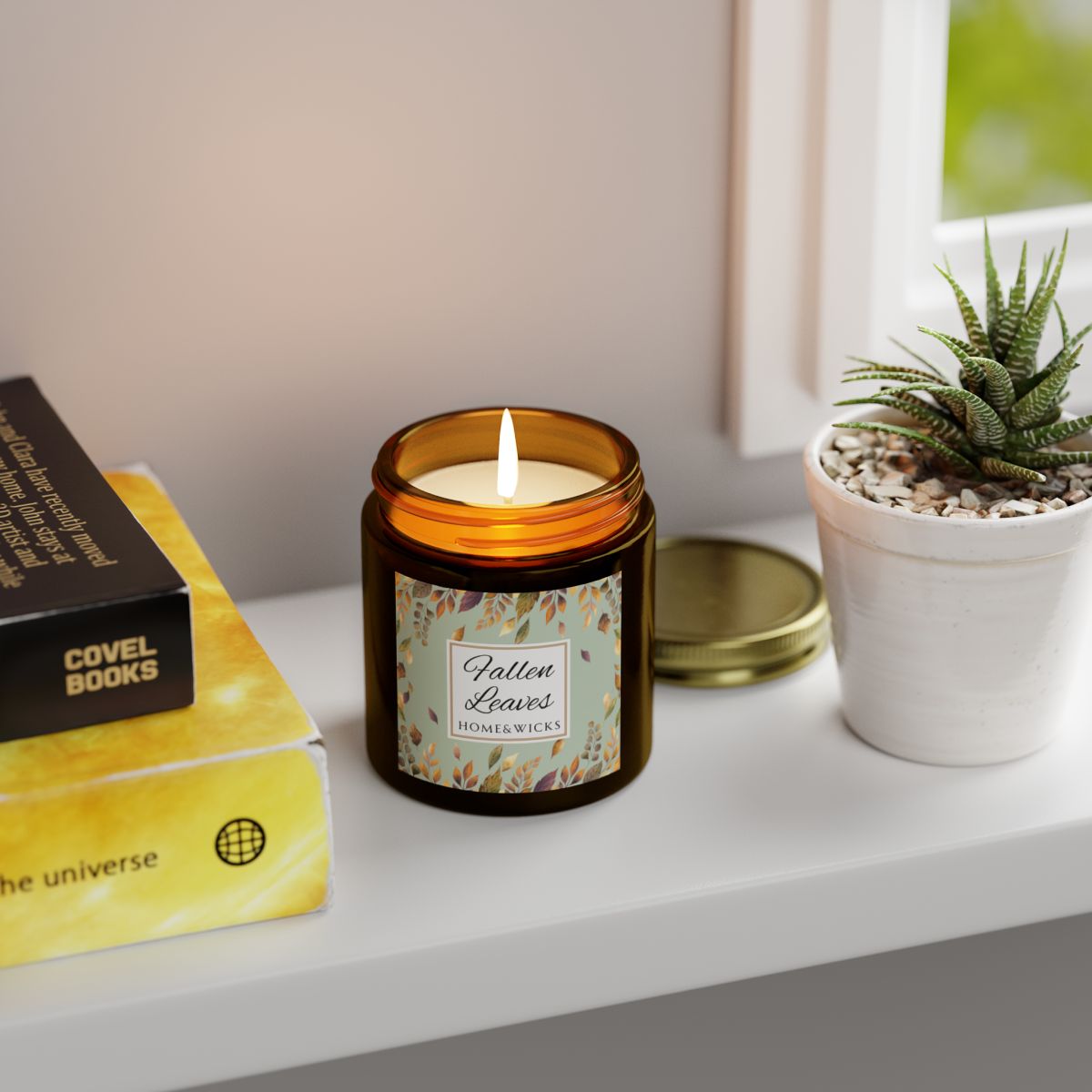Fallen Leaves candle in a 4 oz. amber glass jar with gold lid with a 'Fallen Leaves' label on a white background by Home & Wicks on a shelf with books and a plant