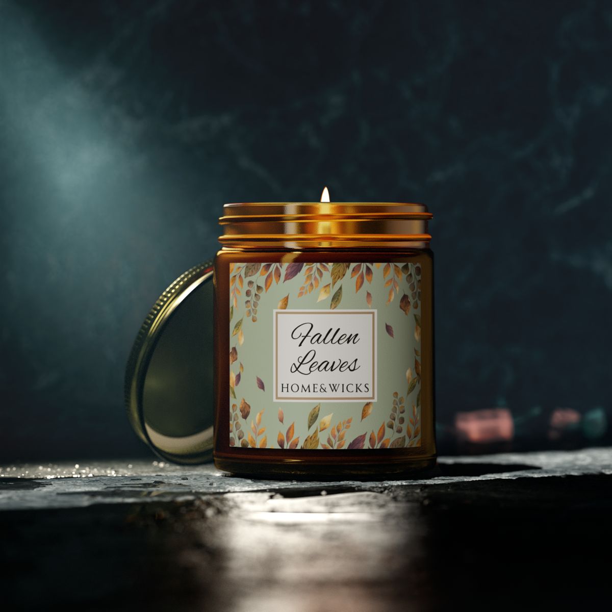 Amber glass candle jar with gold lid with brown, gold and green 'Fallen Leaves' label on a white background by Home & Wicks on a dark background