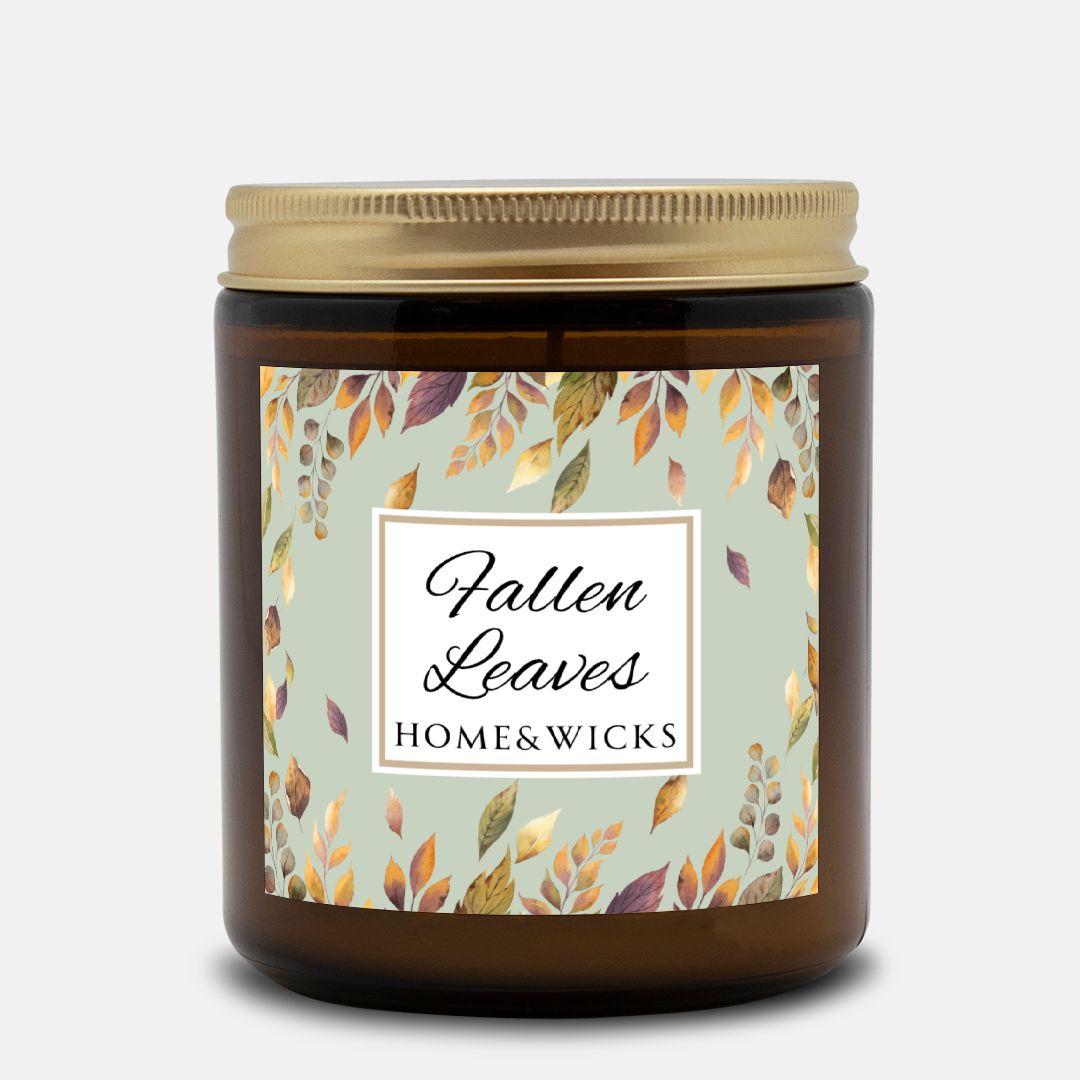 Amber glass candle jar with a gold lid with a brown, gold and green 'Fallen Leaves' label on a white background by Home & Wicks