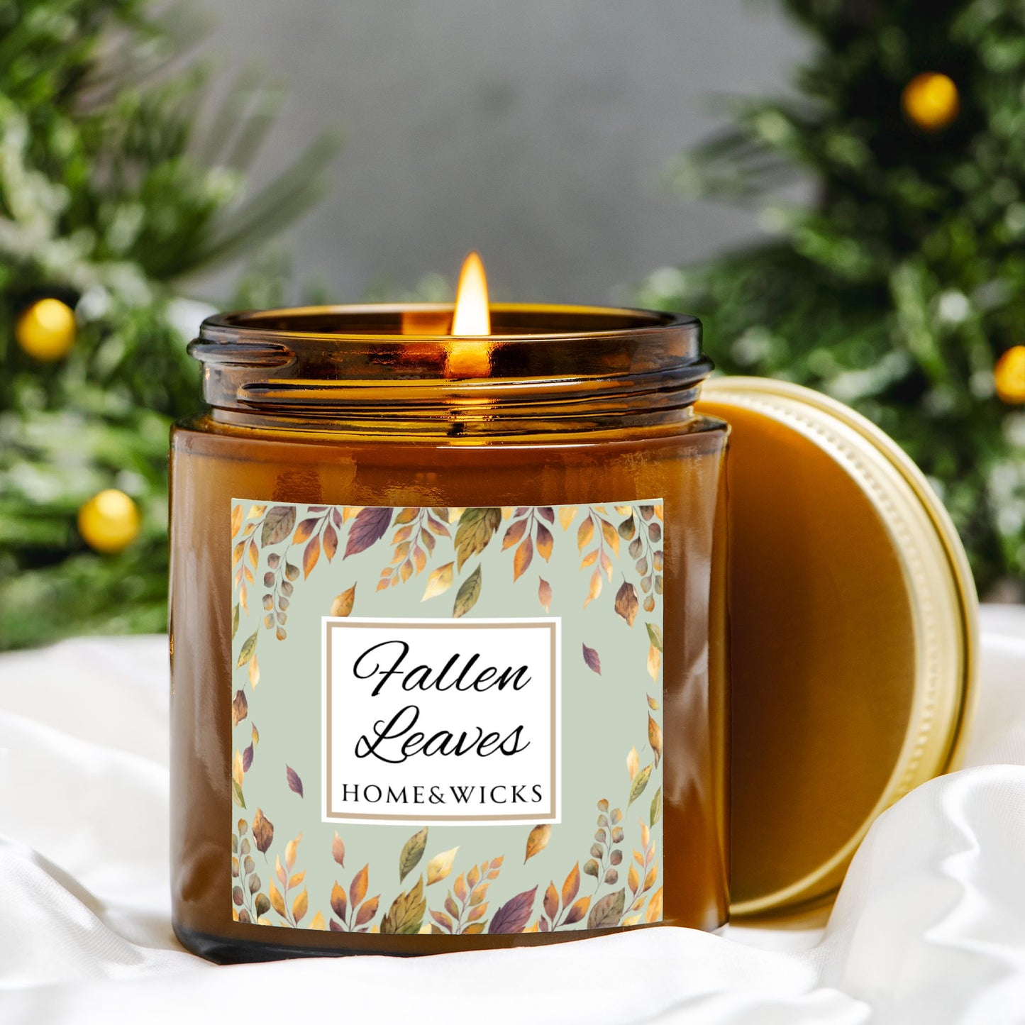 Fallen Leaves candle in a 4 oz. amber glass jar with gold lid with a 'Fallen Leaves' label on a white background by Home & Wicks with a decorative orange tree background