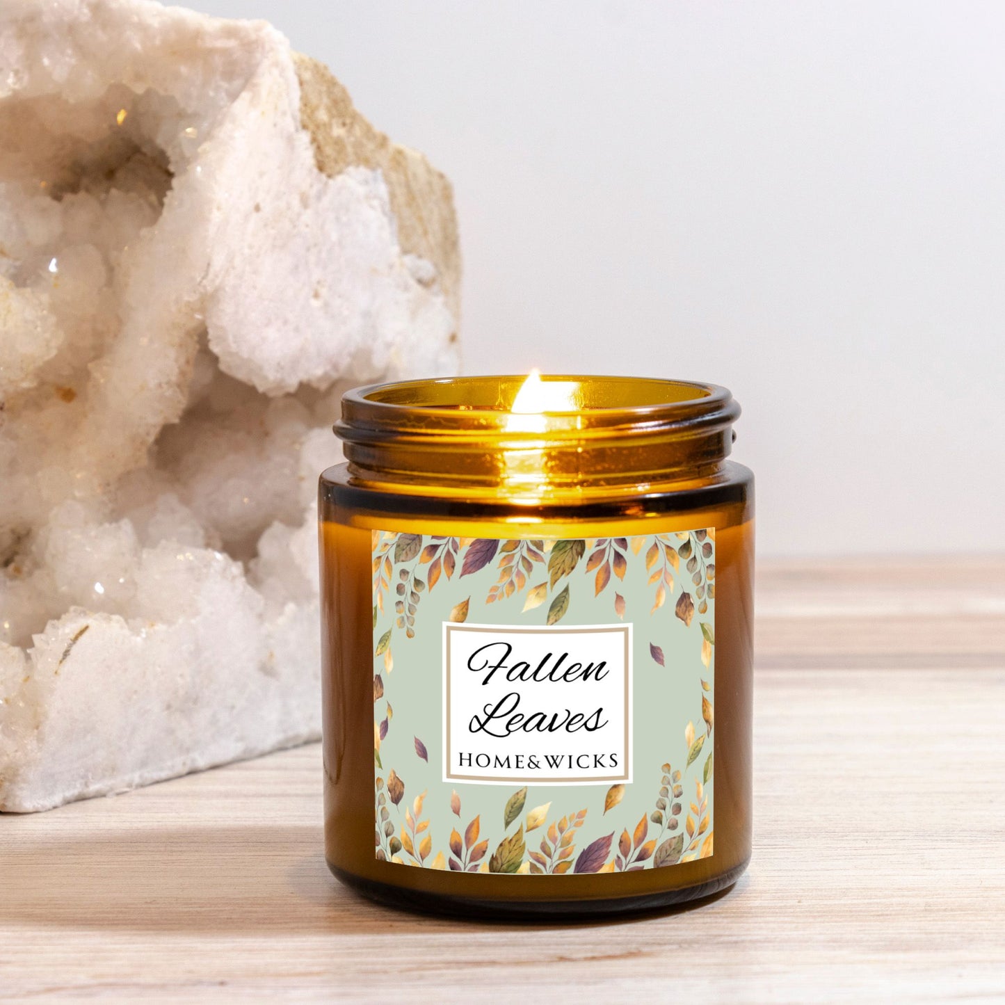 Fallen Leaves candle in a 4 oz. amber glass jar with gold lid with a 'Fallen Leaves' label on a white background by Home & Wicks on a wooden surface with a white background