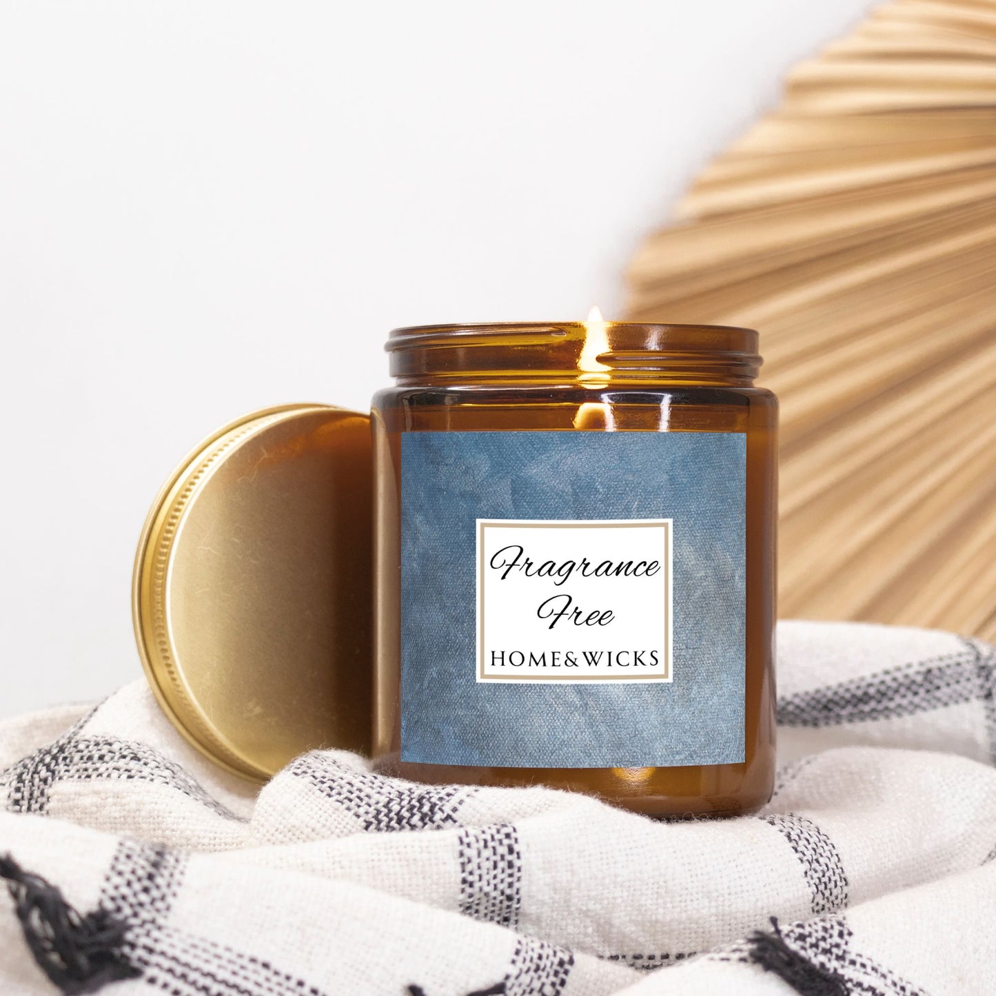 Unscented Candle in an amber jar with gold lid with 'Fragrance Free' label on a denim blue background on a white and black patterned blanket background