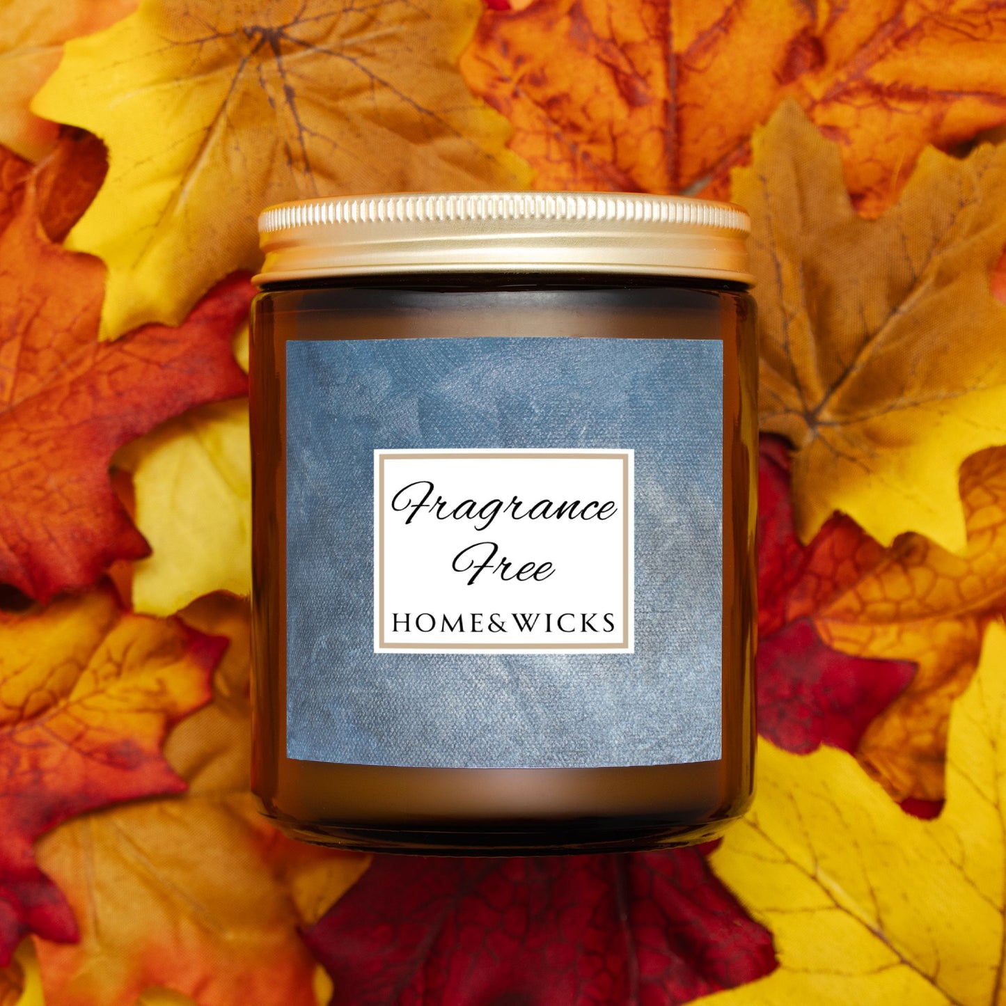 Unscented Candle in an amber jar with gold lid with with a 'Fragrance Free' label on a bed of autumn leaves