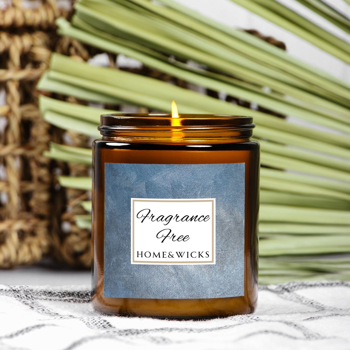 Unscented Candle in an amber jar with gold lid with 'Fragrance Free' label on a denim blue background with a blue label on a textured surface with green leaves in the background