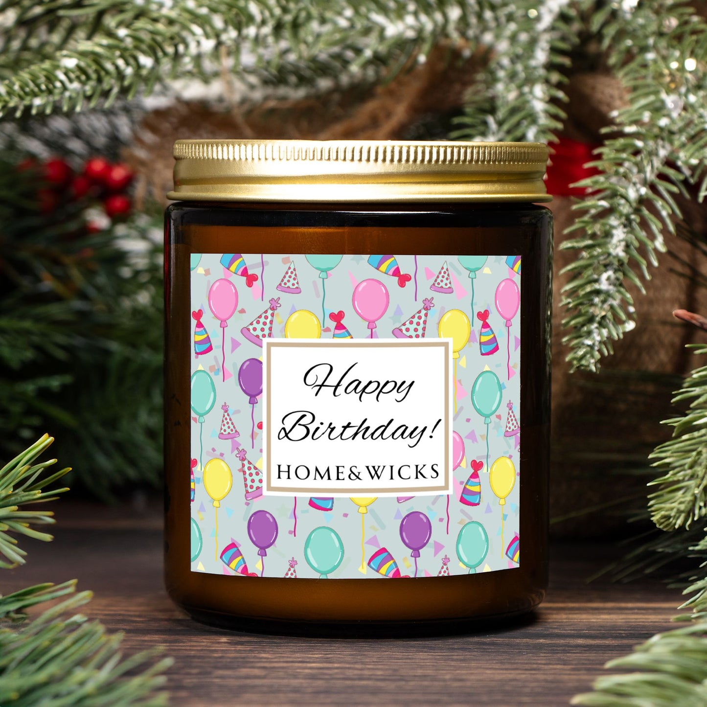 Amber candle jar with gold label with a 'Happy Birthday' label and colorful design with birthday balloons, birthday hats and confetti background in front of Christmas trees