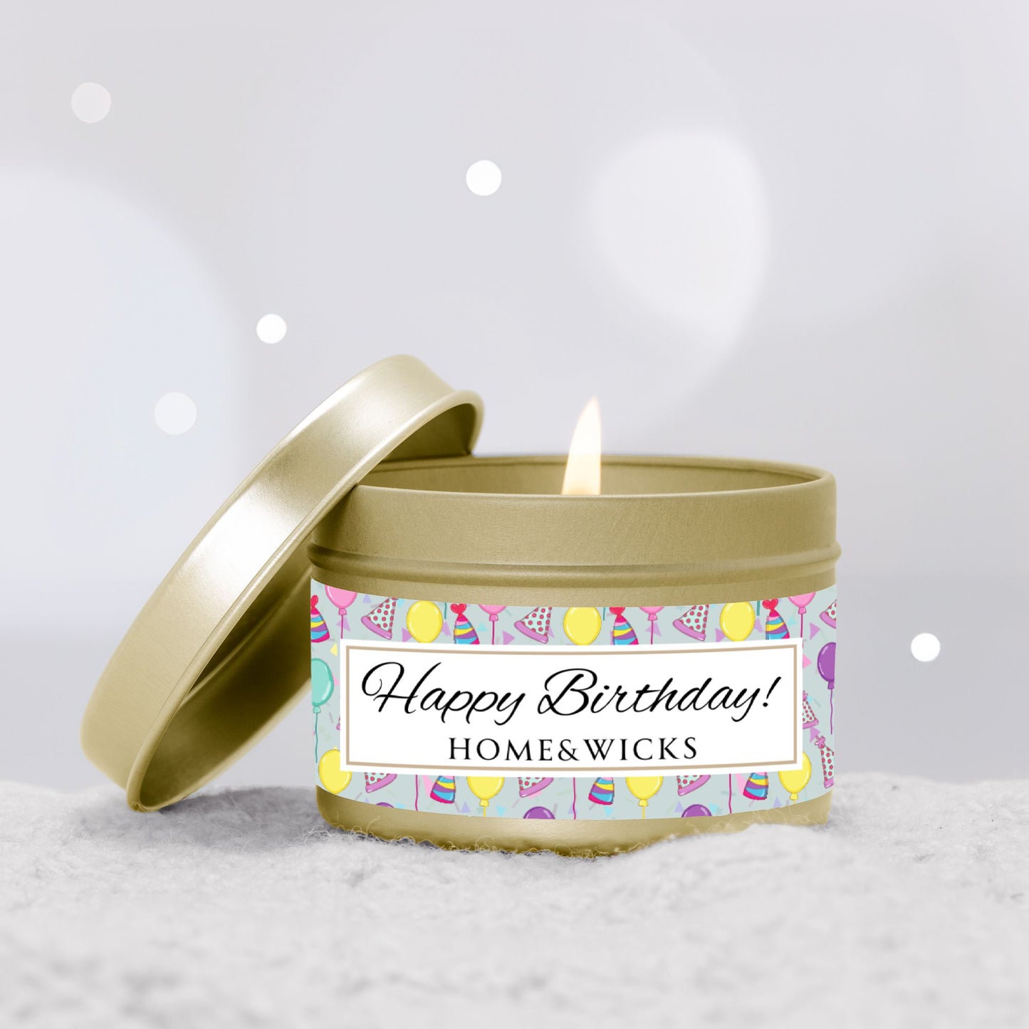 Happy Birthday gold 4 oz. candle tin with gold lid with a colorful label with birthday hats, balloons and confetti on a light gray background