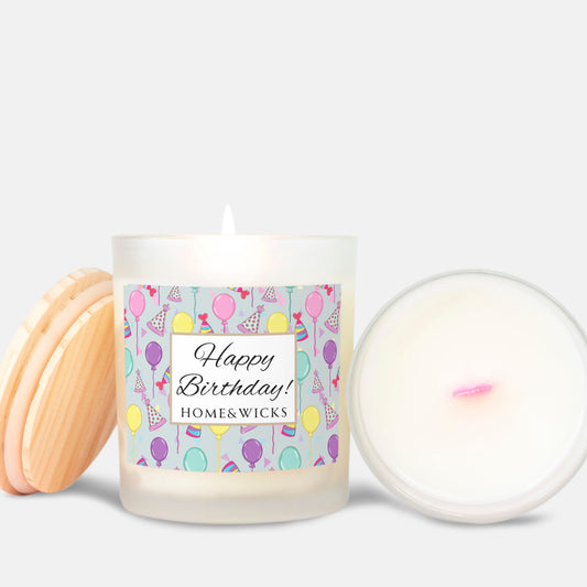Pink wick candle in a frosted jar with bamboo wood lid and with a 'Happy Birthday' label with birthday balloons, birthday hats and confetti by Home & Wicks on a white background