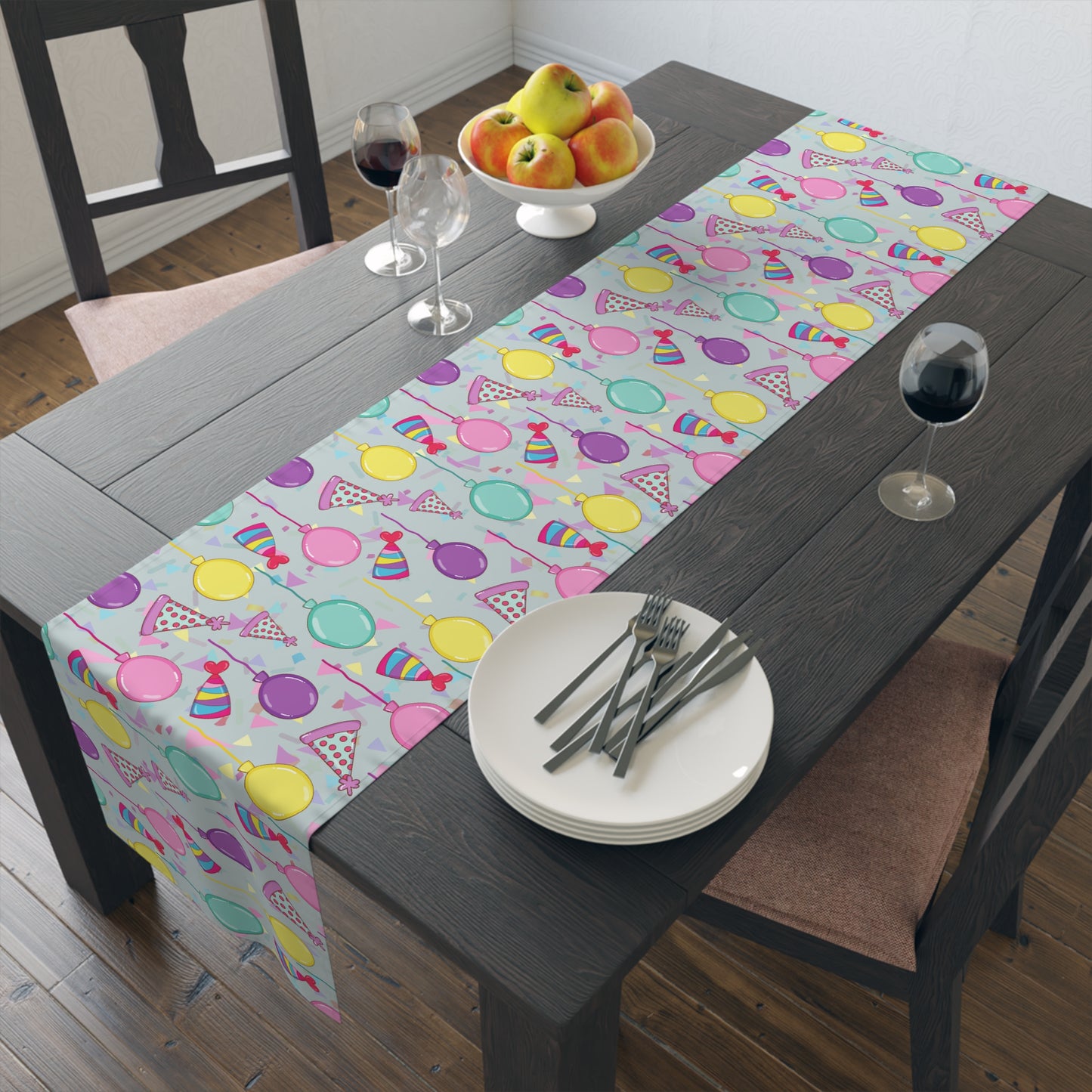 Dining table with a Table runner with colorful birthday party hats, confetti and balloons pattern patterned table runner, plates, and cutlery.