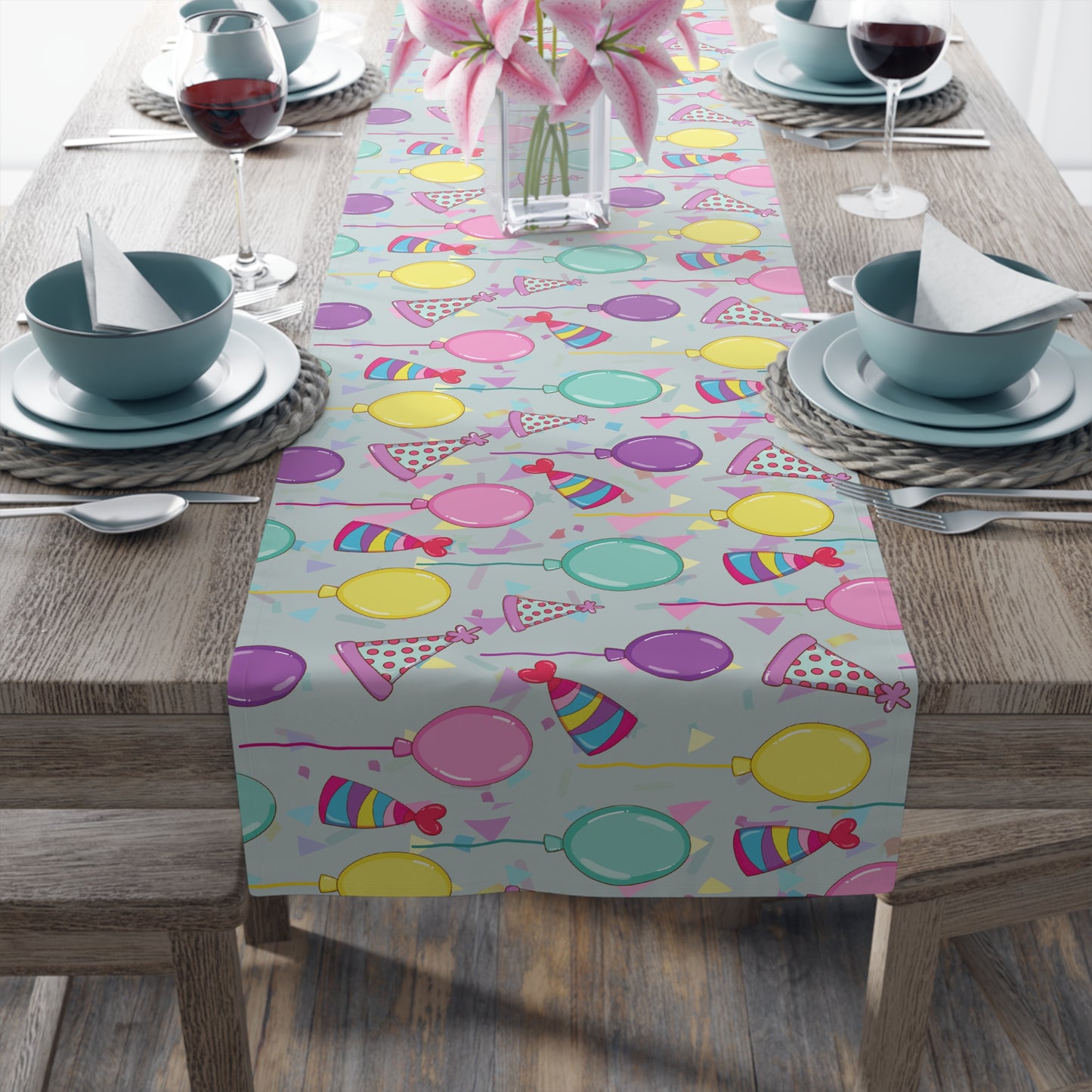 Table setting with a Table runner with colorful birthday party hats, confetti and balloons pattern on a wooden table.