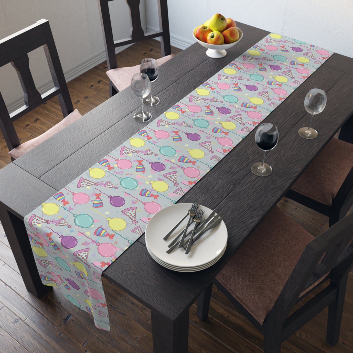Dining table with a table runner with colorful birthday party hats, confetti and balloons pattern colorful patterned table runner, plates, and glasses.