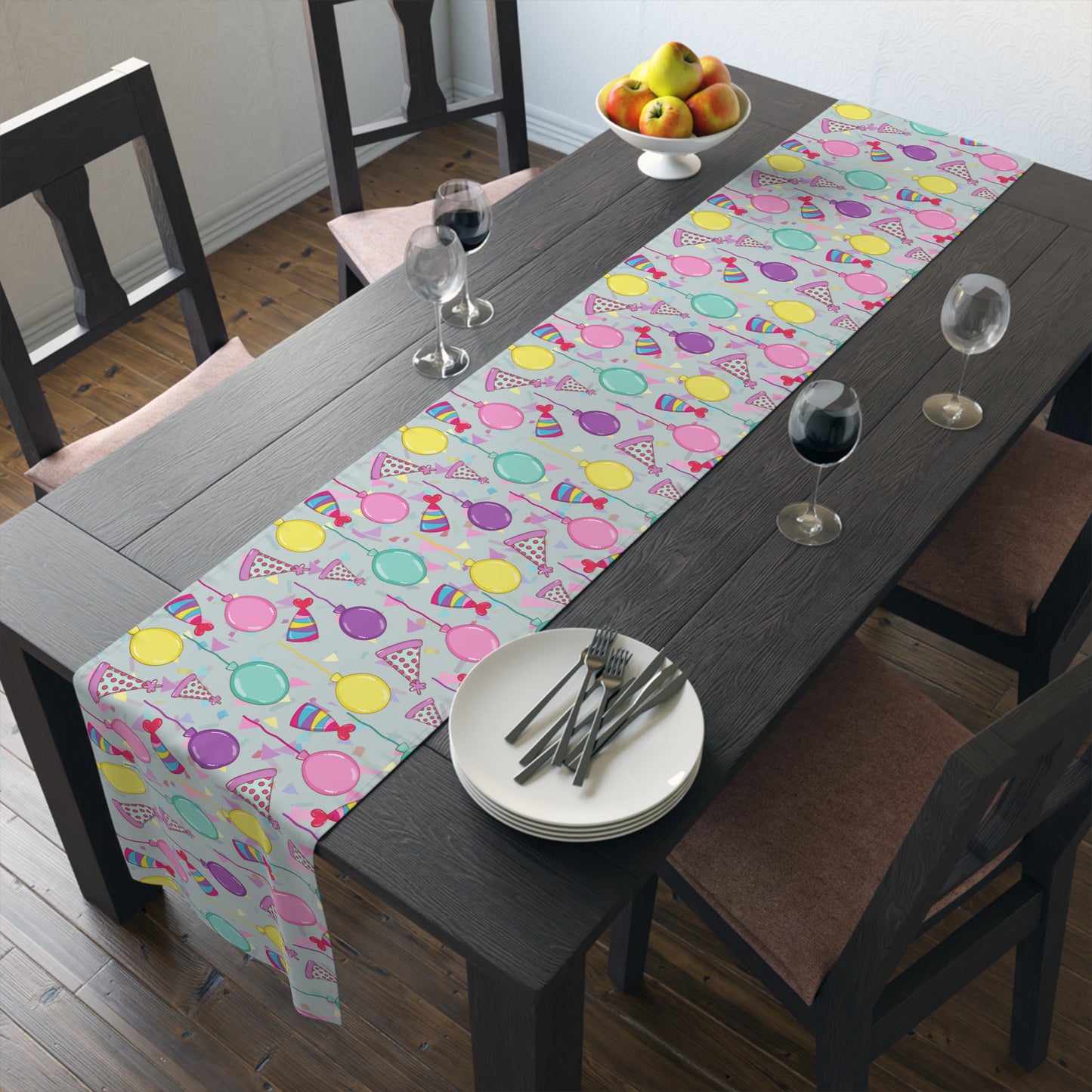 Dining table with a Table runner with colorful birthday party hats, confetti and balloons patterned table runner, plates, and glasses.