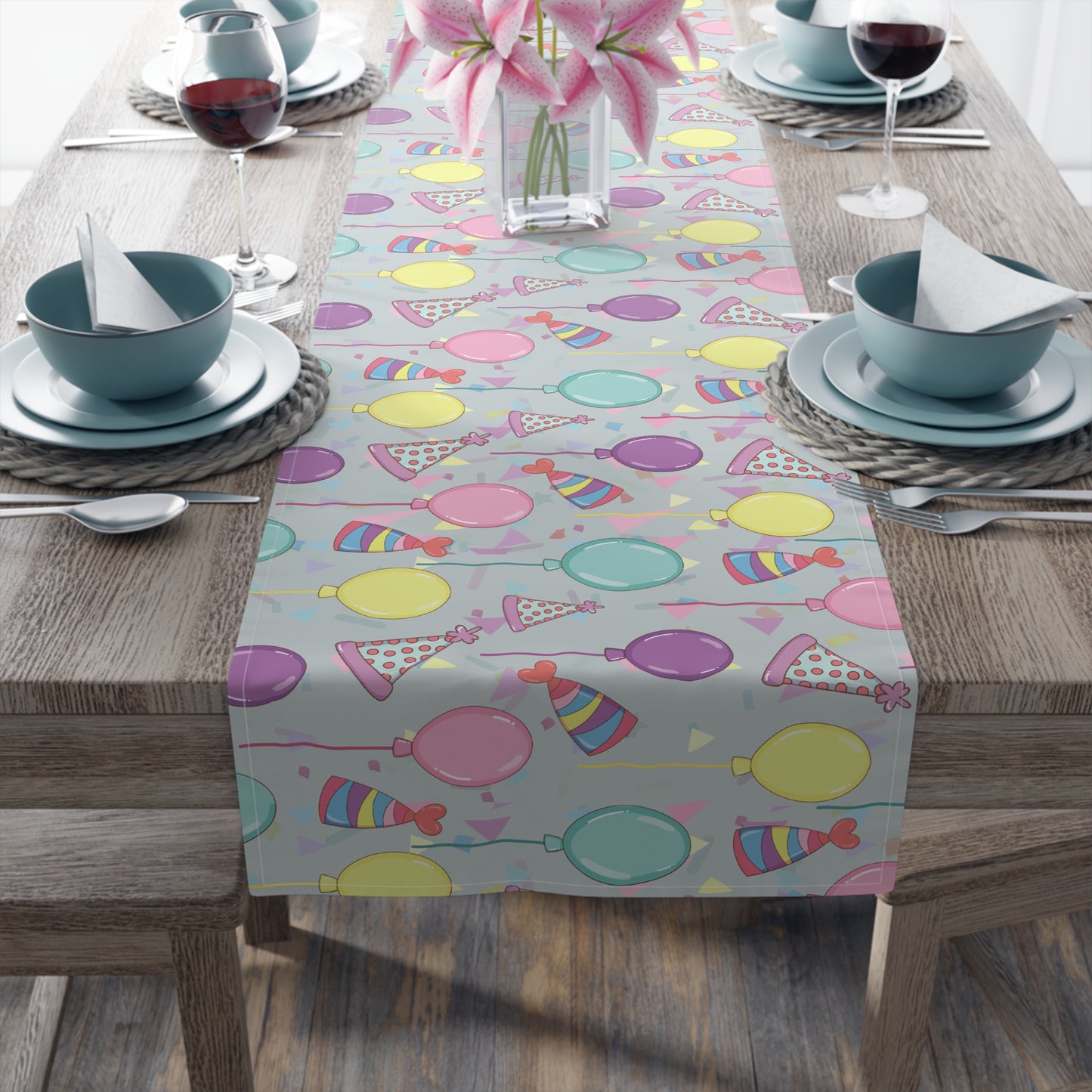 Table setting with a table runner with colorful birthday party hats, confetti and balloons pattern on a wooden table.