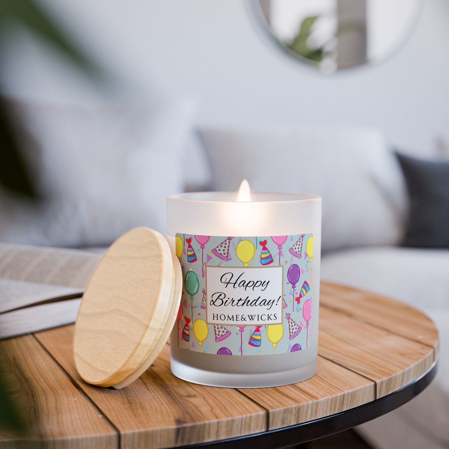 Lit wood wick candle with a 'Happy Birthday' label featuring balloons and party hats with maple wood lid on a white background.on a wooden table