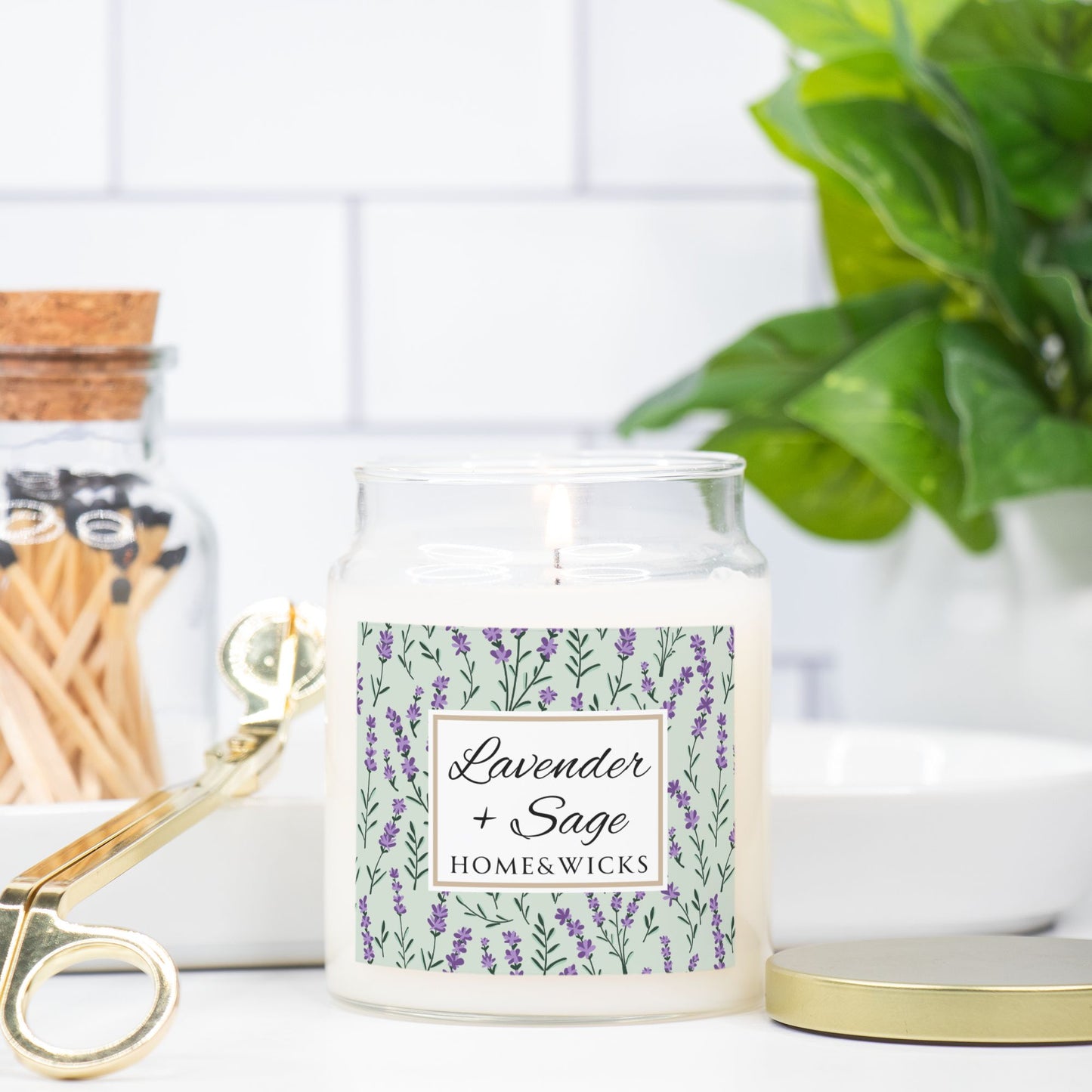 Homewares item with a candle labeled 'Lavender + Sage' from Homewicks, placed on a surface with a plant and matches in the background.