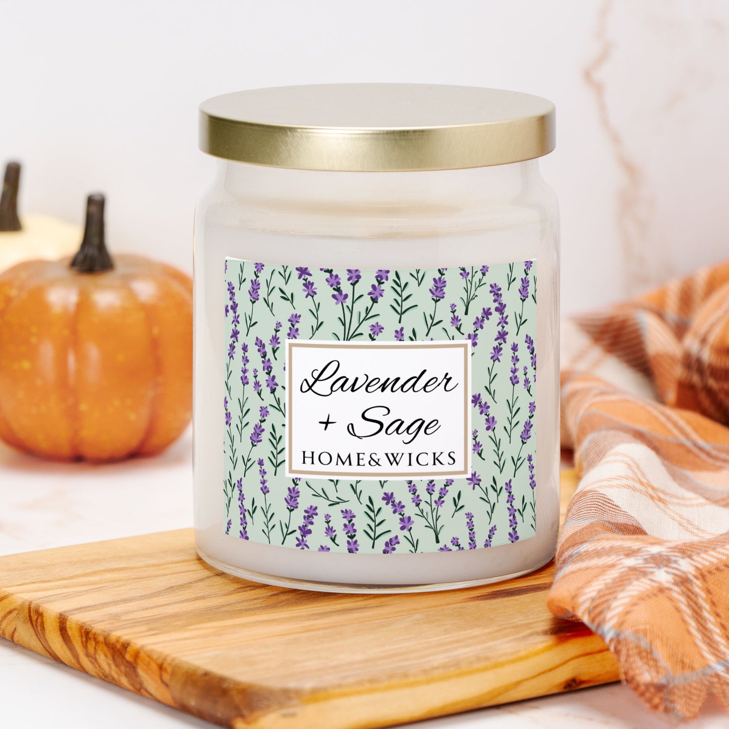 Candle jar labeled 'Lavender + Sage' by Home & Wicks on a wooden board with a pumpkin and plaid fabric in the background.