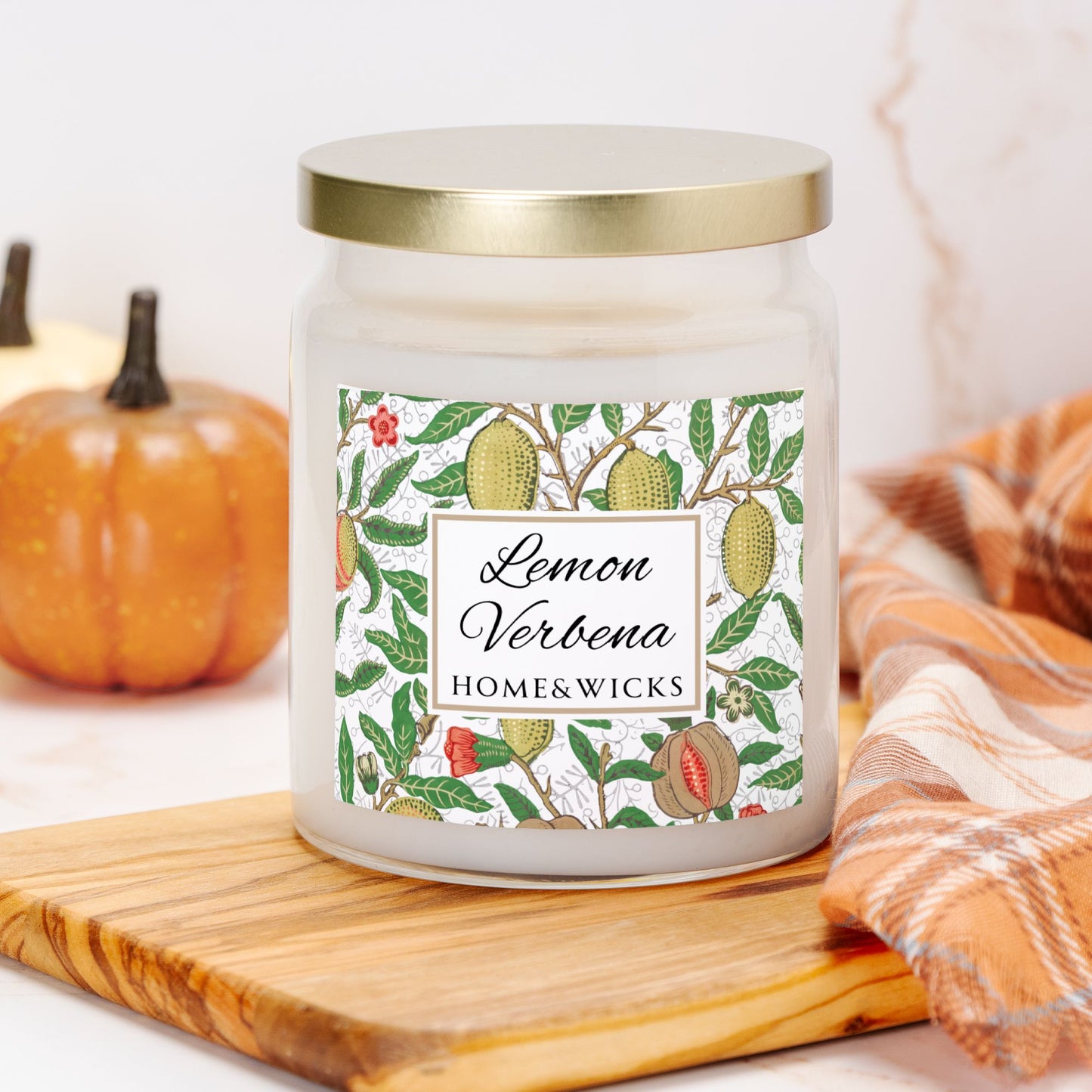 Candle jar labeled 'Lemon Verbena' by Home & Wicks on a wooden board with pumpkins and a towel in the background.