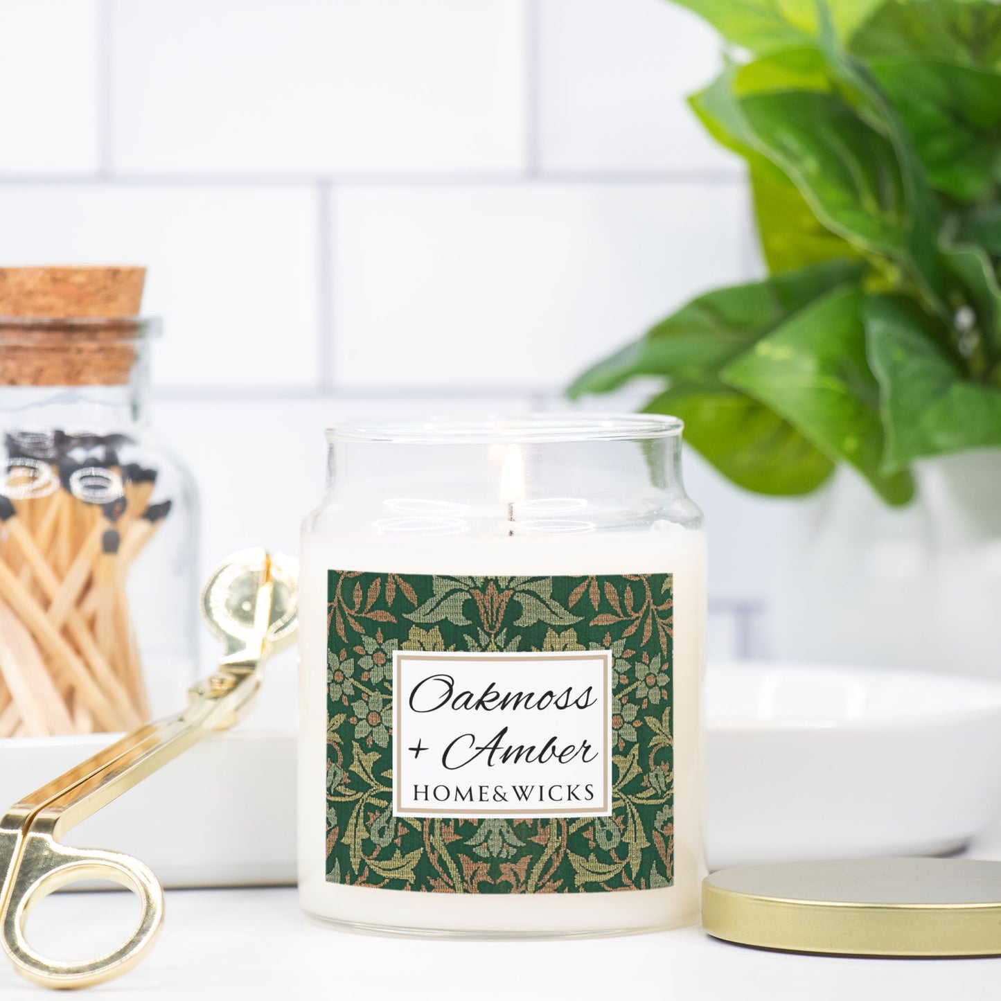 Candle jar with 'Oakmoss + Amber' label on a white surface with decorative elements.