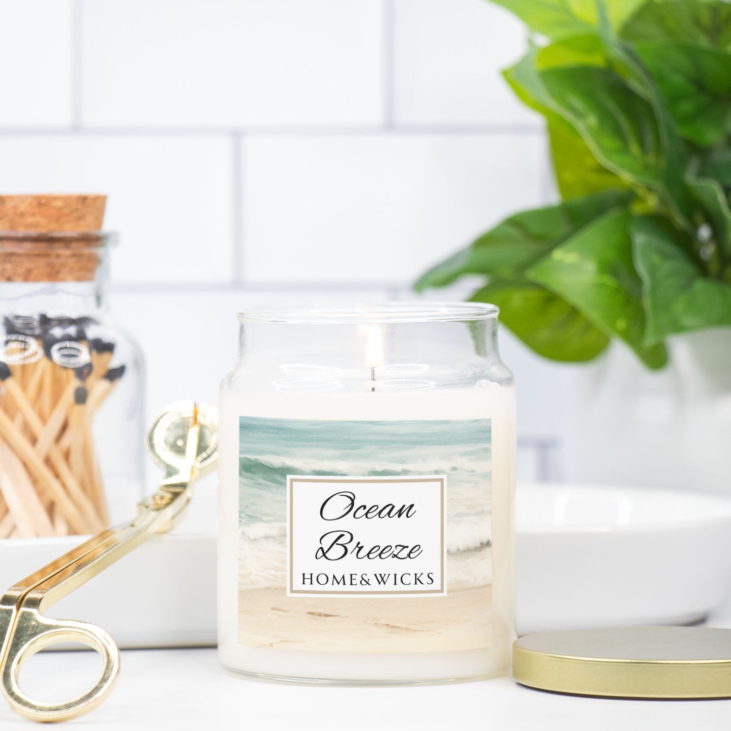 Candle jar labeled 'Ocean Breeze' by Home & Wicks on a surface with a plant and matches in the background.