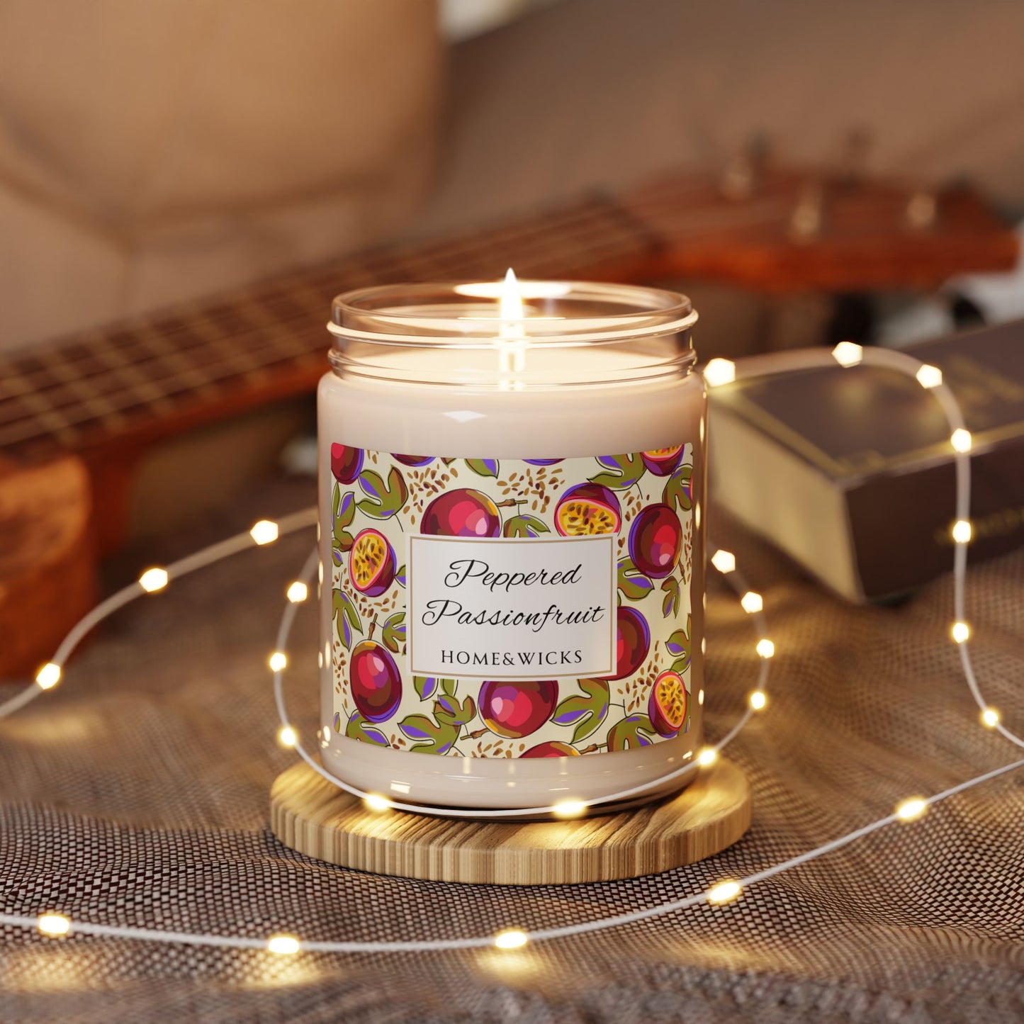 Candle with a decorative peppered passionfruit label on a wooden coaster surrounded by string lights and a guitar in the background