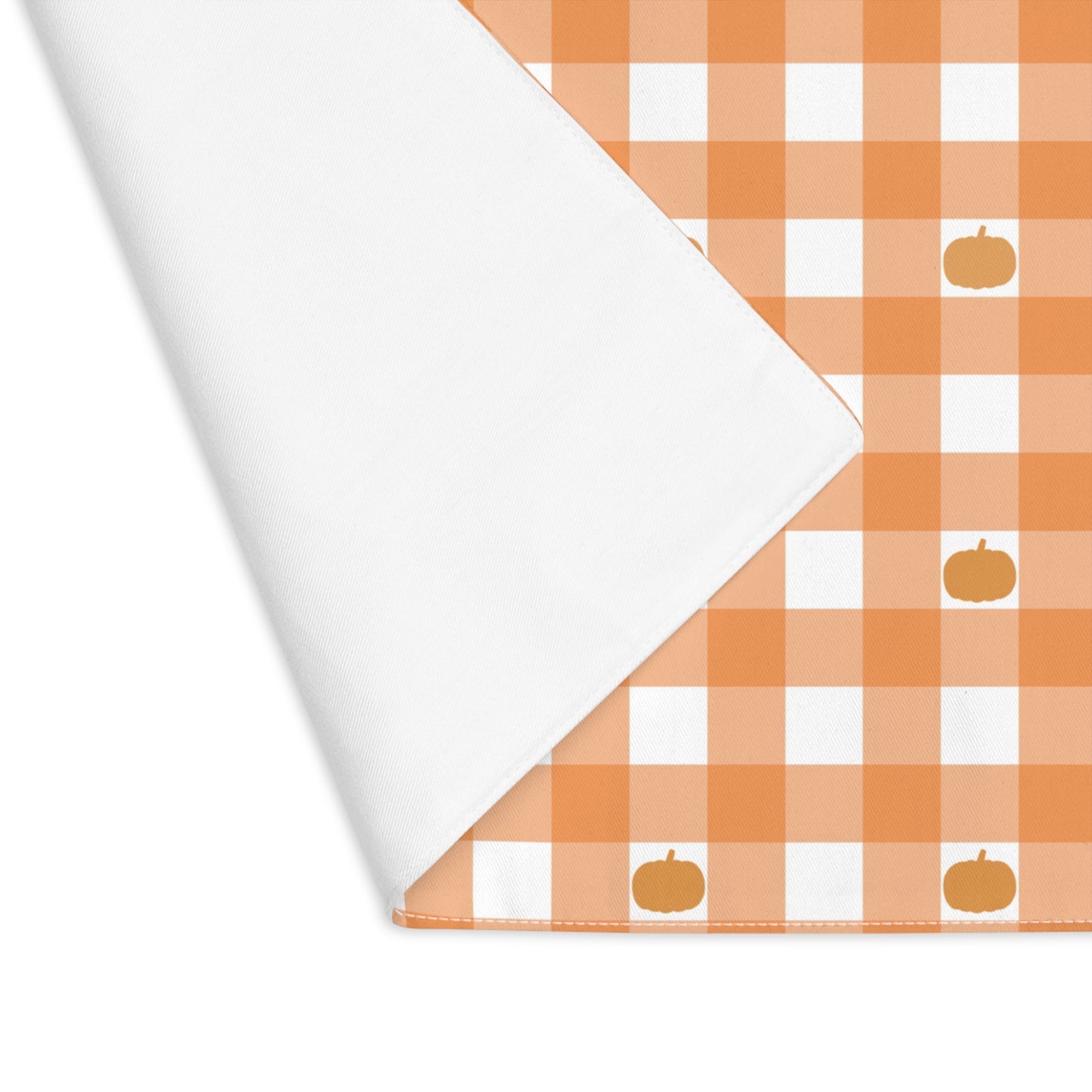 Our Pumpkin Gingham placemat is folded over at the corner to reveal the white back of this orange and white checkered patterned placemat with small pumpkins on the cotton twill placemat fabric on a white background