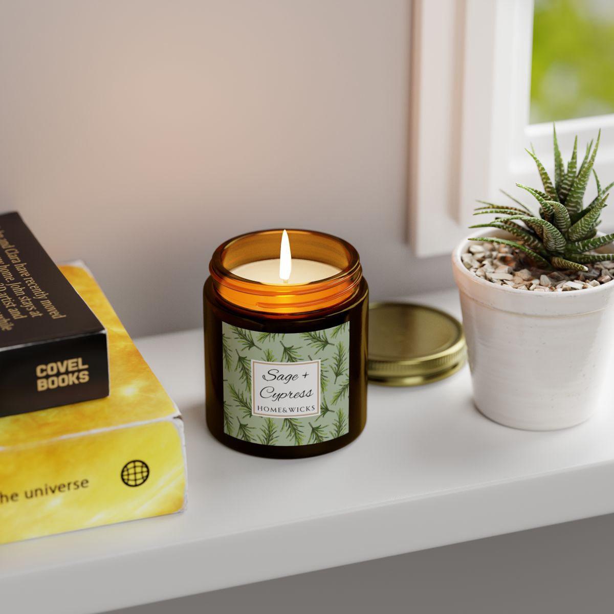 Sage & Cypress candle in a 4 oz. amber glass jar with a gold lid and 'Sage + Cypress' label on a white background by Home & Wicks on a shelf next to books and a plant