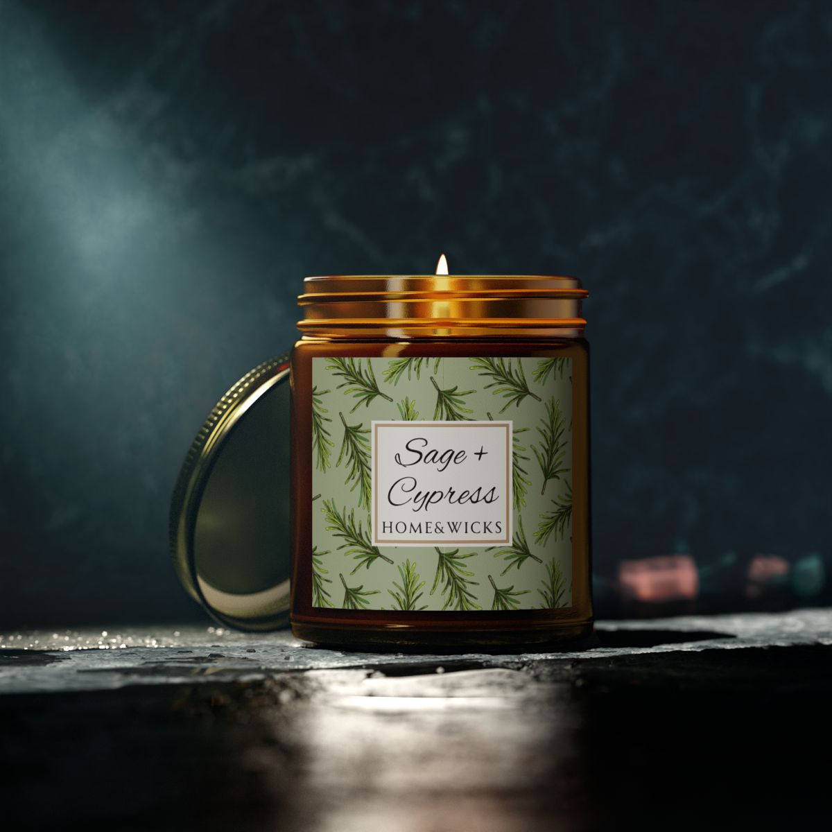 Sage & Cypress candle in an amber jar with gold lid with 'Sage + Cypress' label on a light green background with cypress needle leaves on a dark background