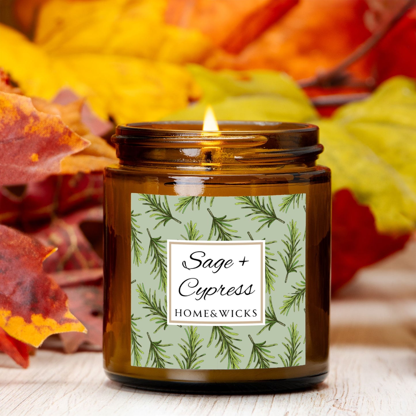 Sage & Cypress candle in a 4 oz. amber glass jar with a gold lid and 'Sage + Cypress' label on a white background by Home & Wicks surrounded by autumn leaves.