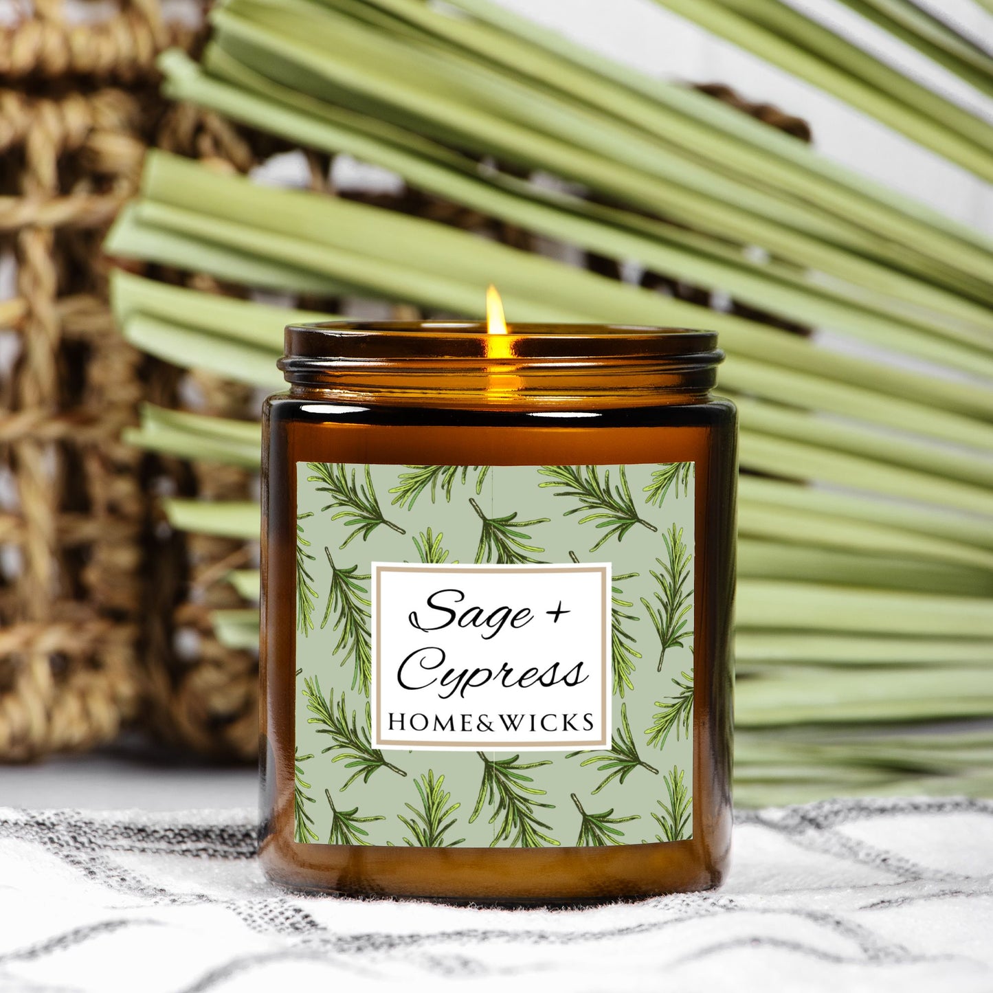 Sage & Cypress candle in an amber jar with gold lid with 'Sage + Cypress' label on a light green background with cypress needle leaves surrounded by greenery.